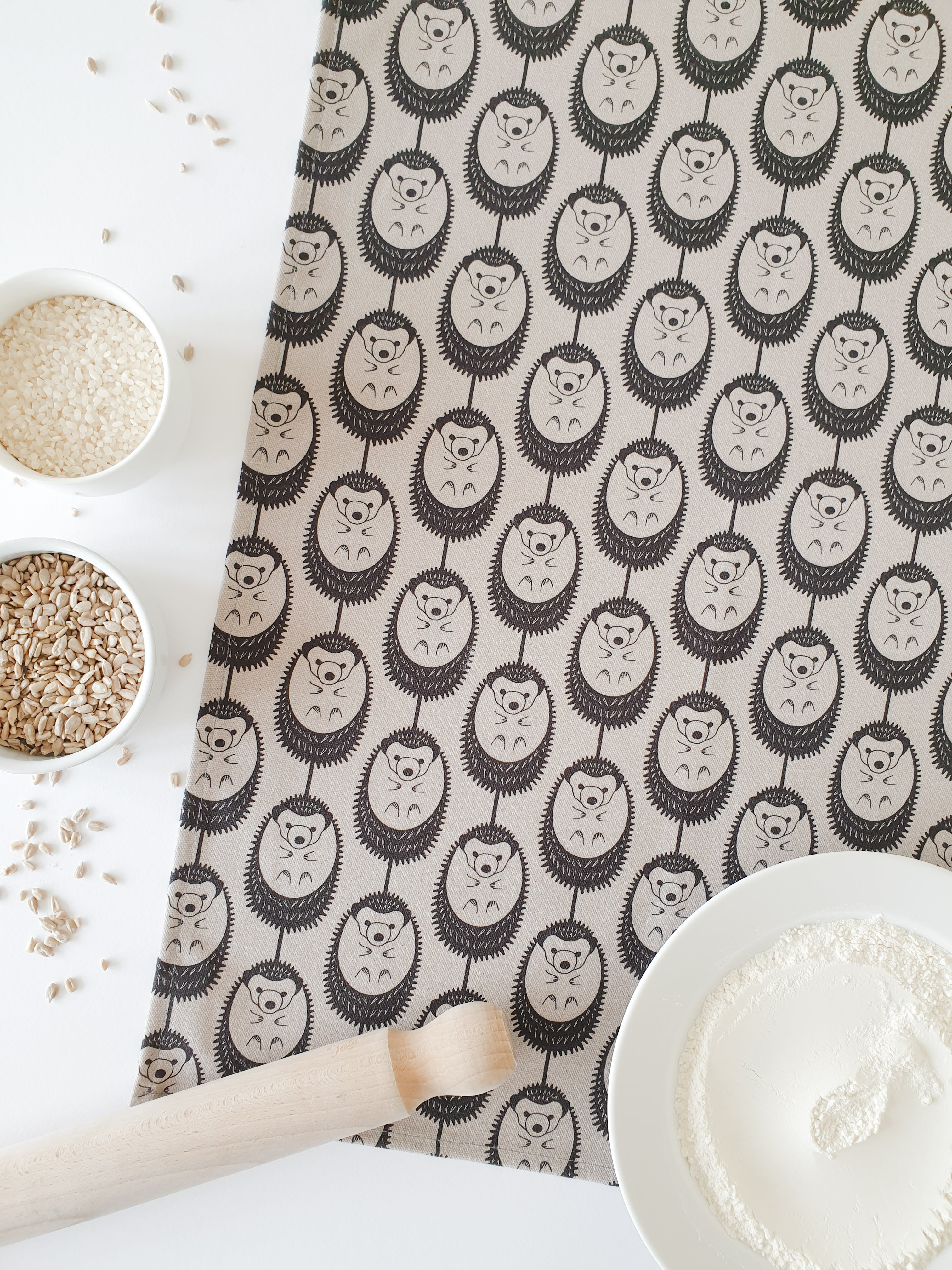 Organic cotton grey hedgehog tea towel – designed by Hannah Issi and handmade in the UK. Stylish, sustainable kitchen linen shown with flour and cooking ingredients.