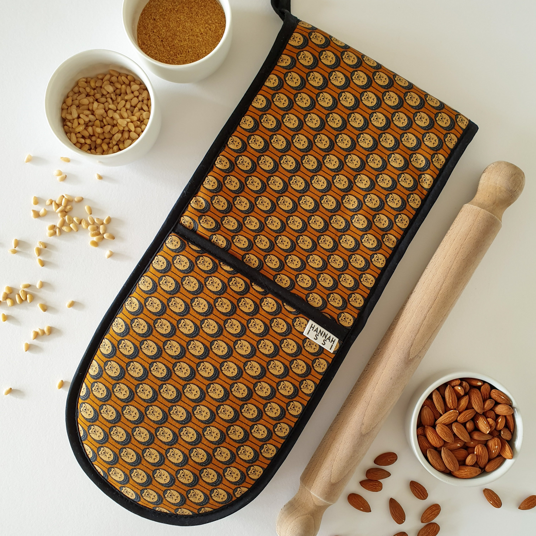 Double oven glove with a hedgehog pattern in autumn colours, wooden rolling pin, and bowls of nuts on a white surface