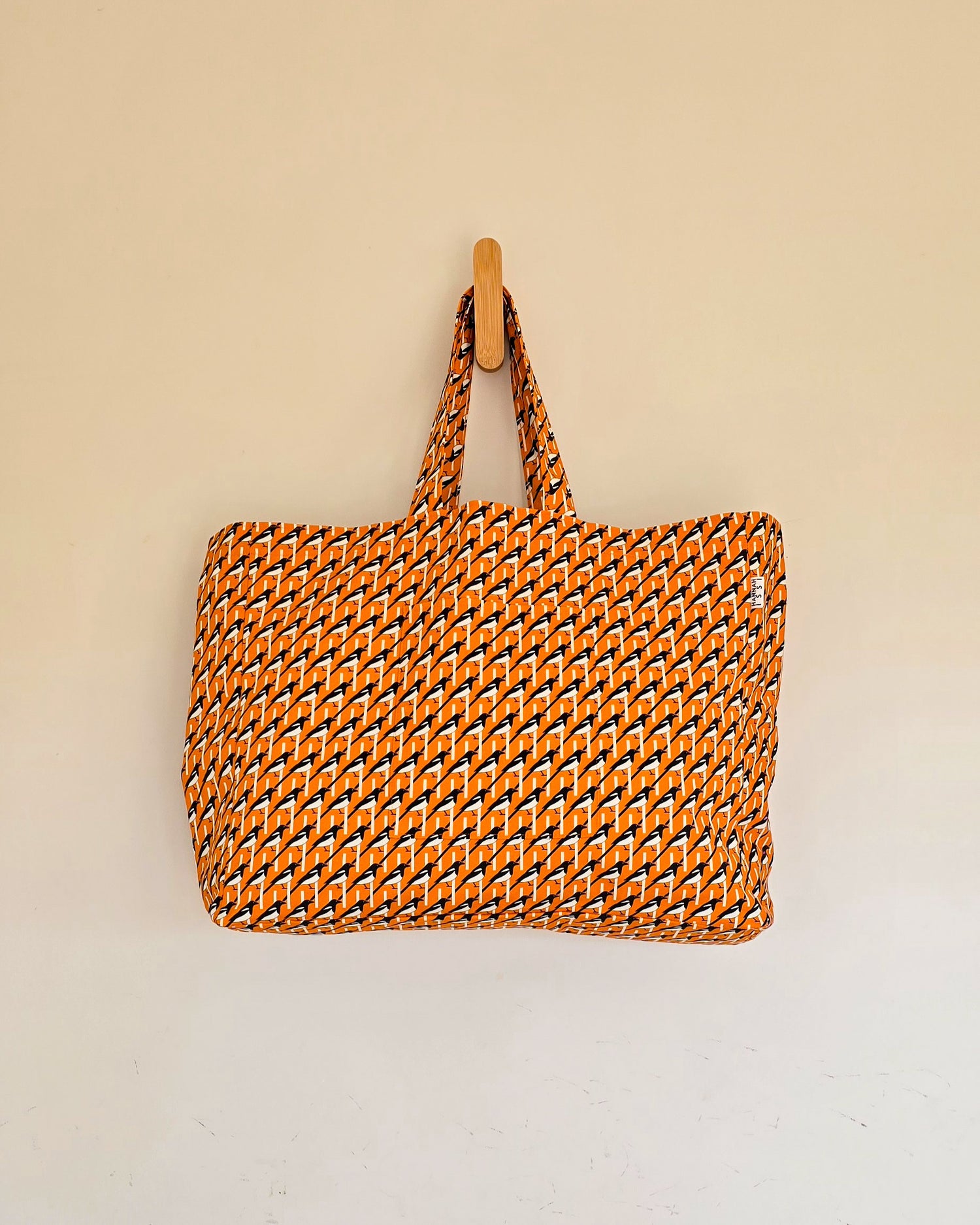 Extra Large oversized orange magpie print shoulder bag pictured hanging on wooden hook on neutral wall - ideal bag for beach, shopping, weekends away and swimming.