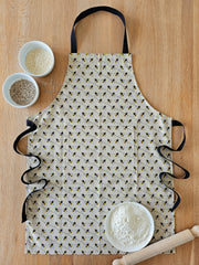 Organic cotton bee apron – designed by Hannah Issi and handmade in the UK. Stylish, sustainable kitchen accessory - apron pictured on wooden tabletop with cooking ingredients.
