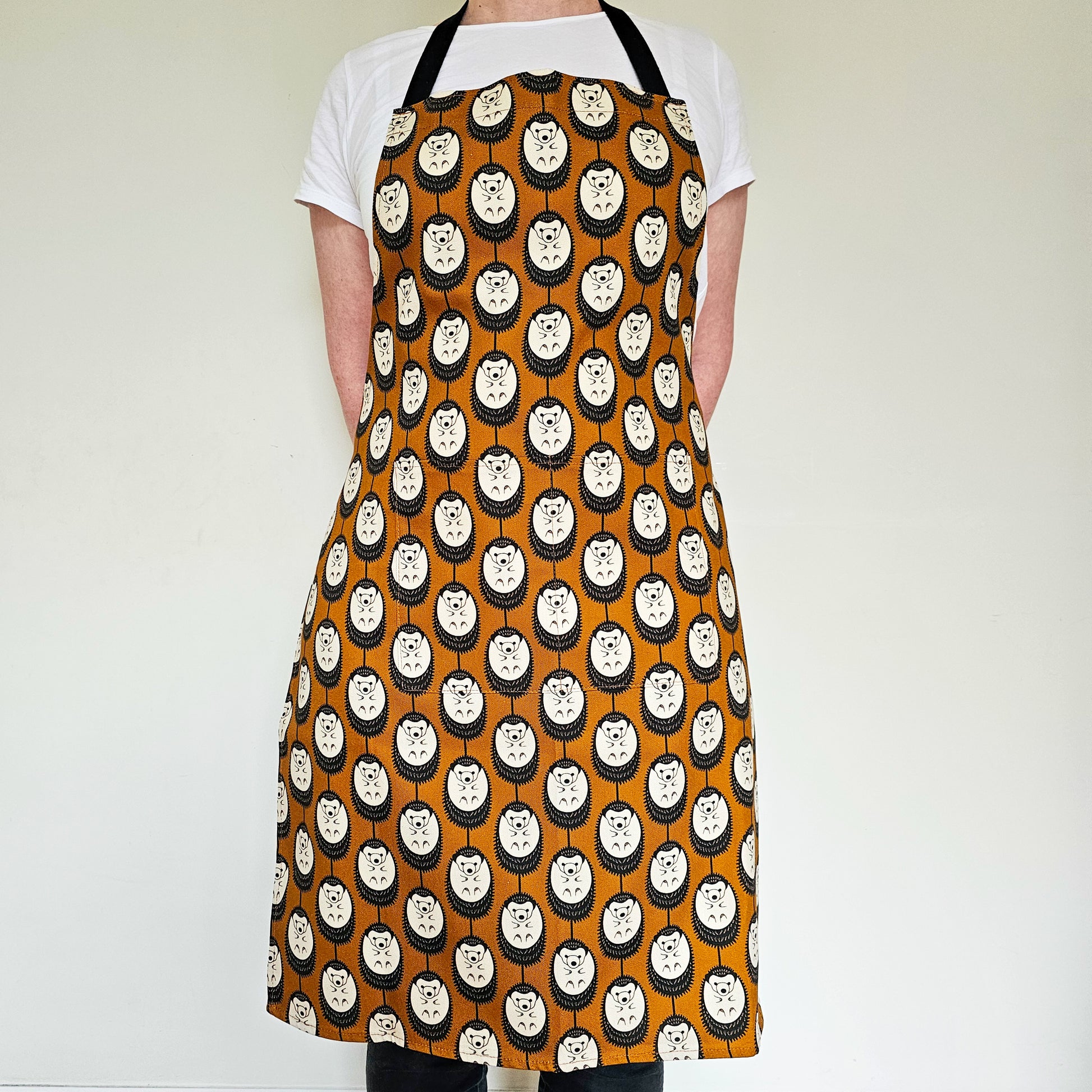 Organic cotton brown and white hedgehog apron – designed by Hannah Issi and handmade in the UK. Stylish, sustainable kitchen textile -photo shows person wearing apron.