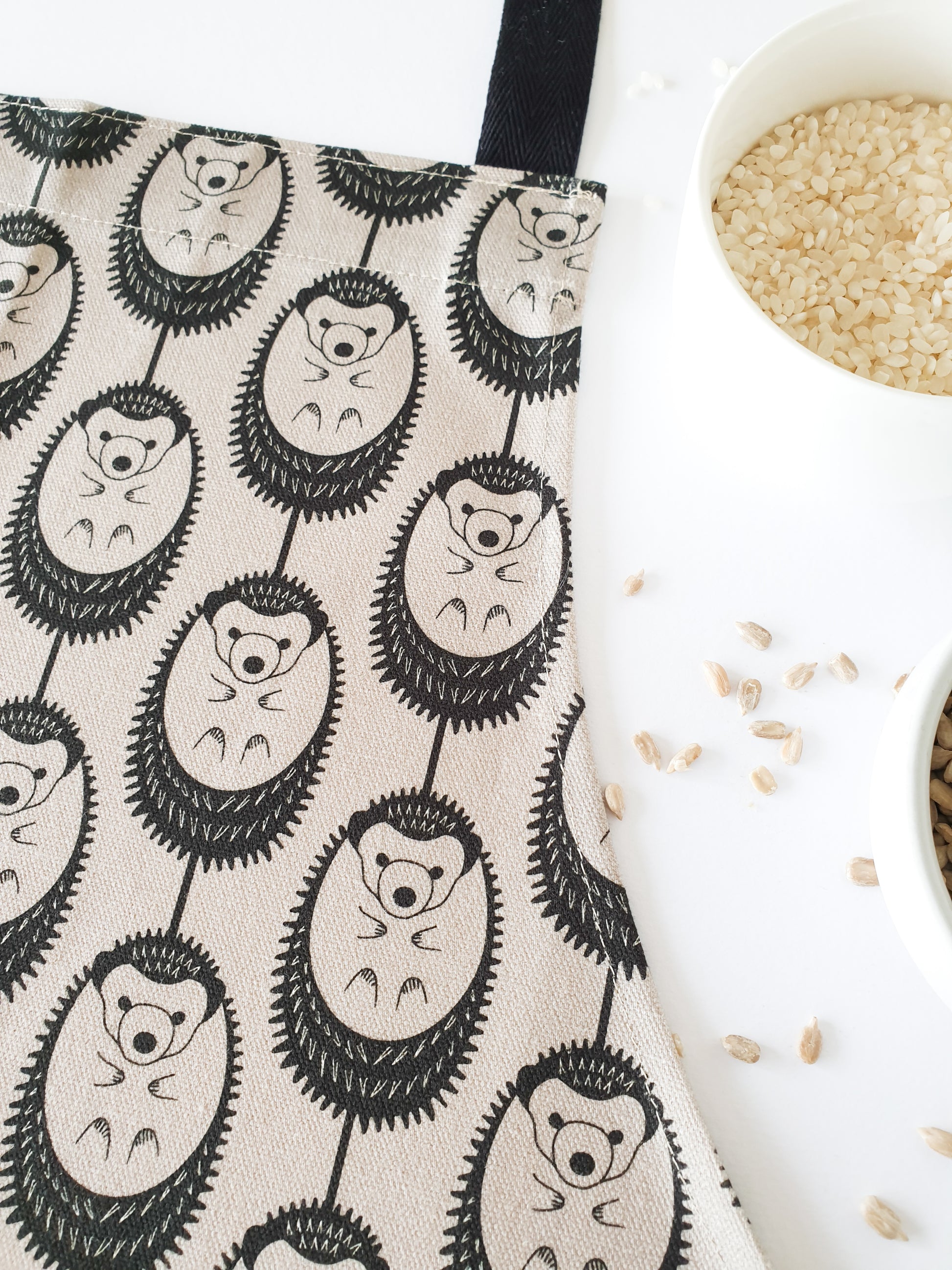 Organic cotton grey hedgehog apron – designed by Hannah Issi and handmade in the UK. Stylish, sustainable kitchen textile. Photo shows close up of print with cooking ingredients. 