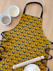 Organic cotton ochre hedgehog apron – designed by Hannah Issi and handmade in the UK. Stylish, sustainable kitchen textile, pictured laying on wooden table with cooking ingredients.