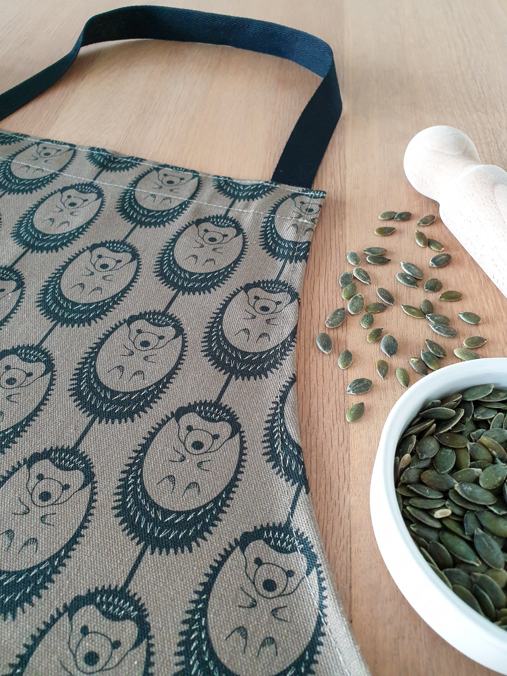 Organic cotton olive green hedgehog apron  – designed by Hannah Issi and handmade in the UK. Stylish, sustainable kitchen accessory - photo of close up detail of print.