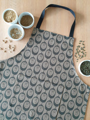 Organic cotton olive green hedgehog apron – designed by Hannah Issi and handmade in the UK. Stylish, sustainable kitchen accessory pictured with cooking ingredients.