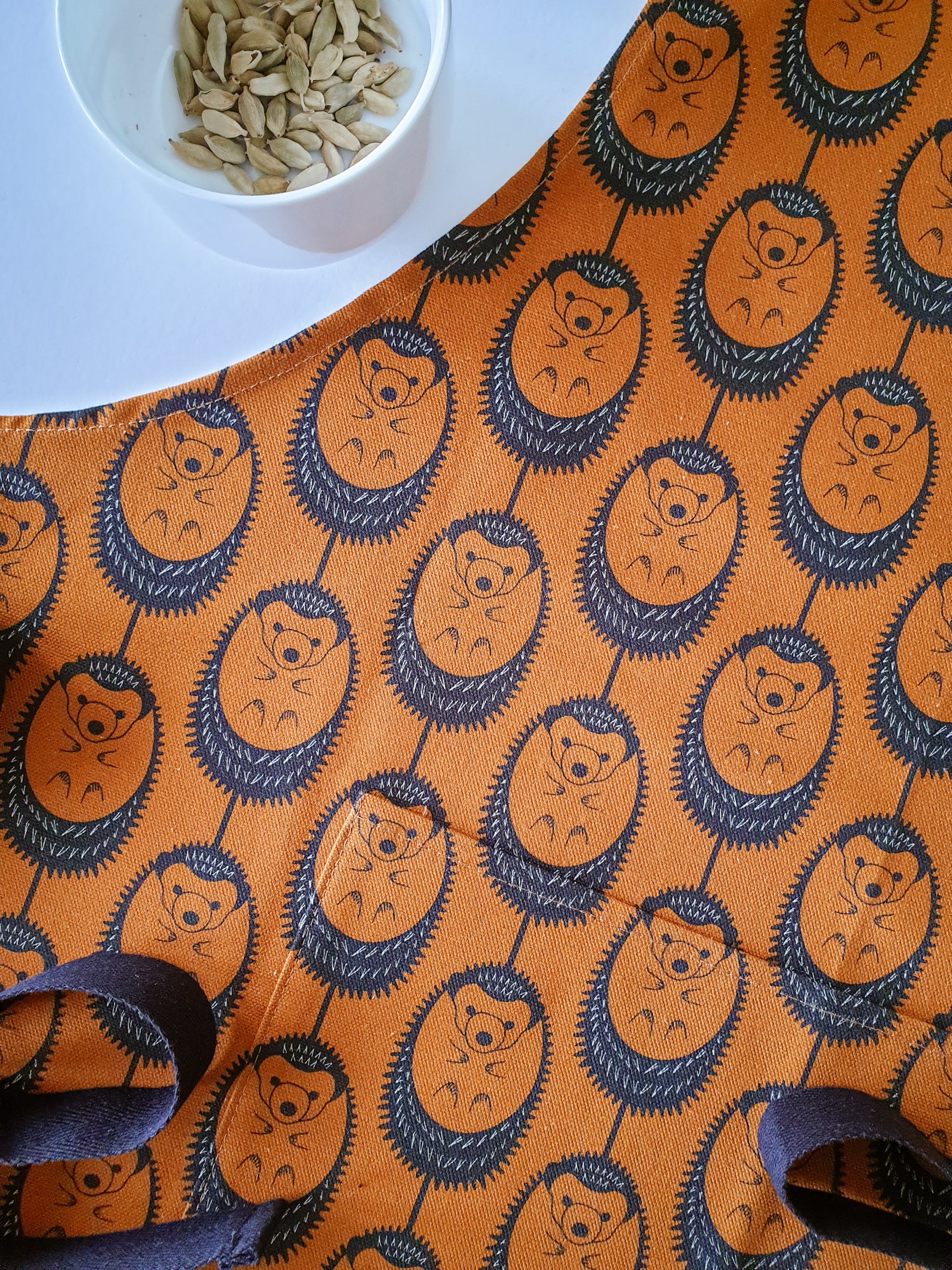 Organic cotton terracotta hedgehog apron – designed by Hannah Issi and handmade in the UK. Sustainable, modern kitchen textile - picture shows close up detail of design with cooking spices.