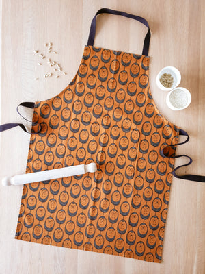 Organic cotton terracotta hedgehog apron – designed by Hannah Issi and handmade in the UK. Sustainable, modern kitchen textile pictured on wooden table with cooking ingredients.