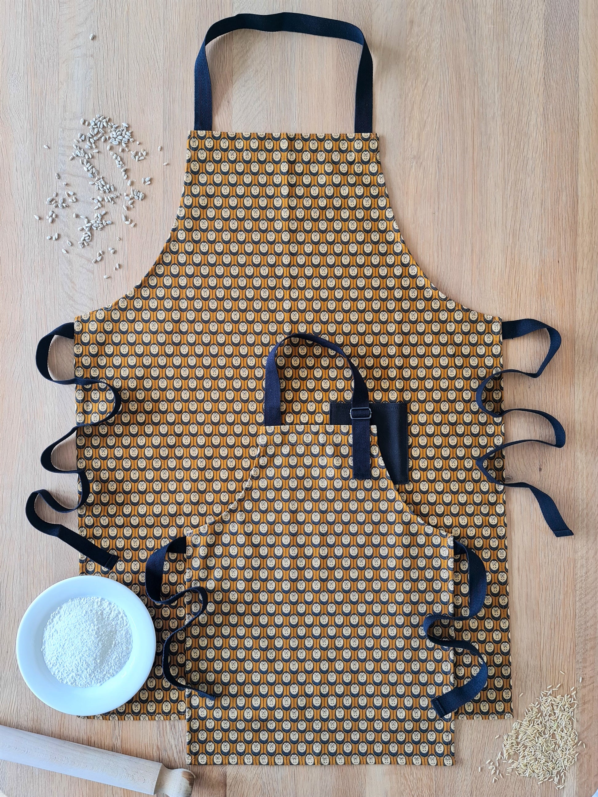 Organic cotton autumn hedgehog apron set (adult & child) – handmade in the UK by Hannah Issi. Stylish, sustainable kitchen pair - pictured on wooden tabletop with cooking ingredients. 