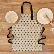 Organic cotton children’s bee apron – handmade in the UK by Hannah Issi. Fun, sustainable kitchen accessory for kids for cooking or messy play. Image shows apron laying on wooden table with cooking ingredients. 
