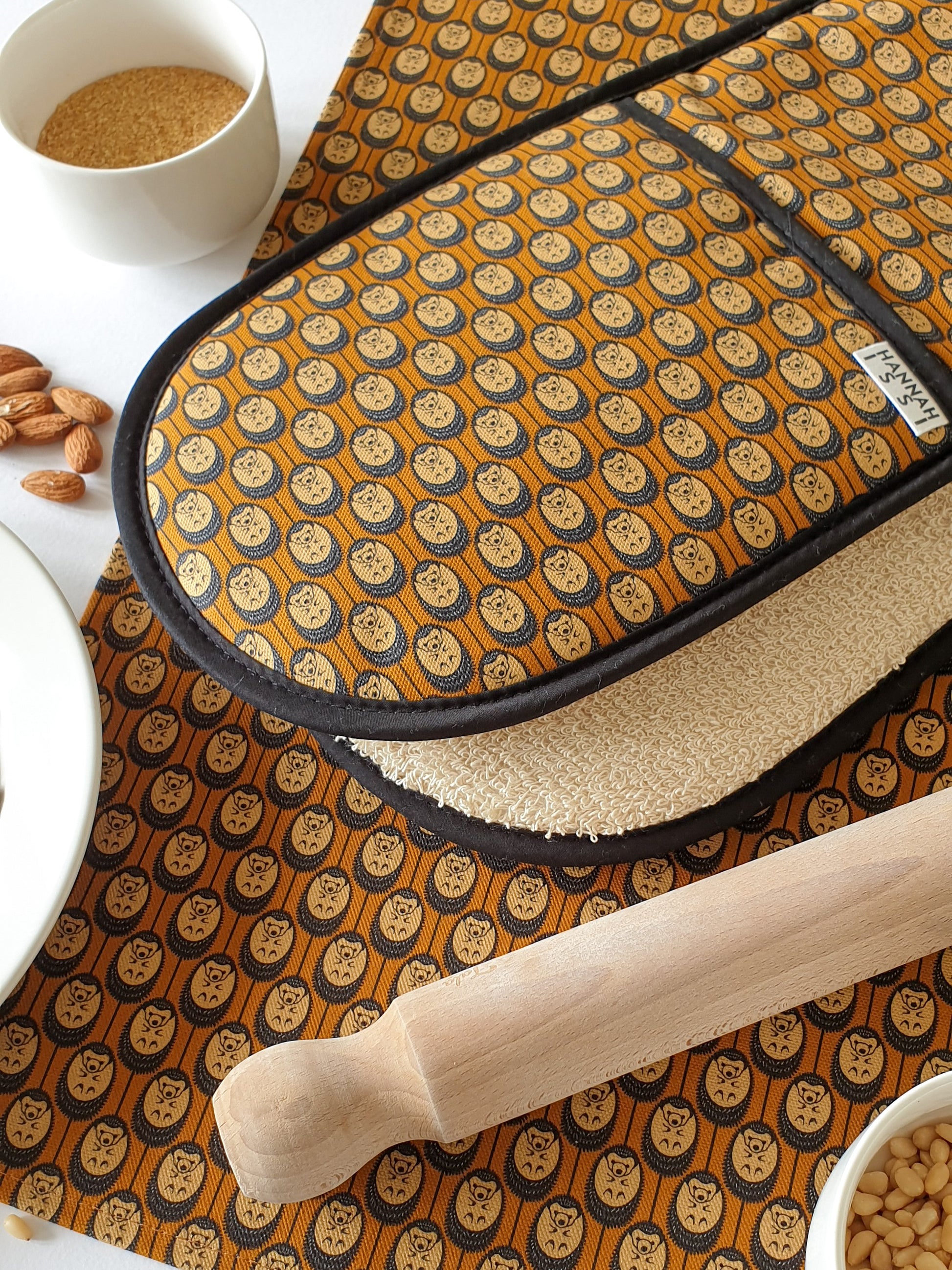 Organic cotton autumn hedgehog double oven glove – handmade in the UK by Hannah Issi. Stylish, heat-safe kitchen accessory. Lifestyle image close-up with matching tea towel, cooking ingredients and rolling pin.