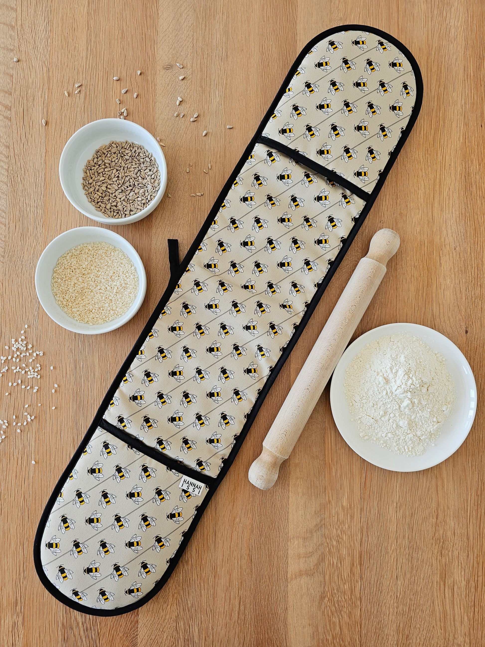 Organic cotton bee double oven glove – handmade in the UK by Hannah Issi. Stylish, heat-safe kitchen accessory. Image has wooden background and cooking ingredients. 