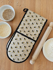 Organic cotton bee double oven glove – handmade in the UK by Hannah Issi. Stylish, heat-safe kitchen accessory. Image shows the glove on wooden tabletop with cooking ingredients. 