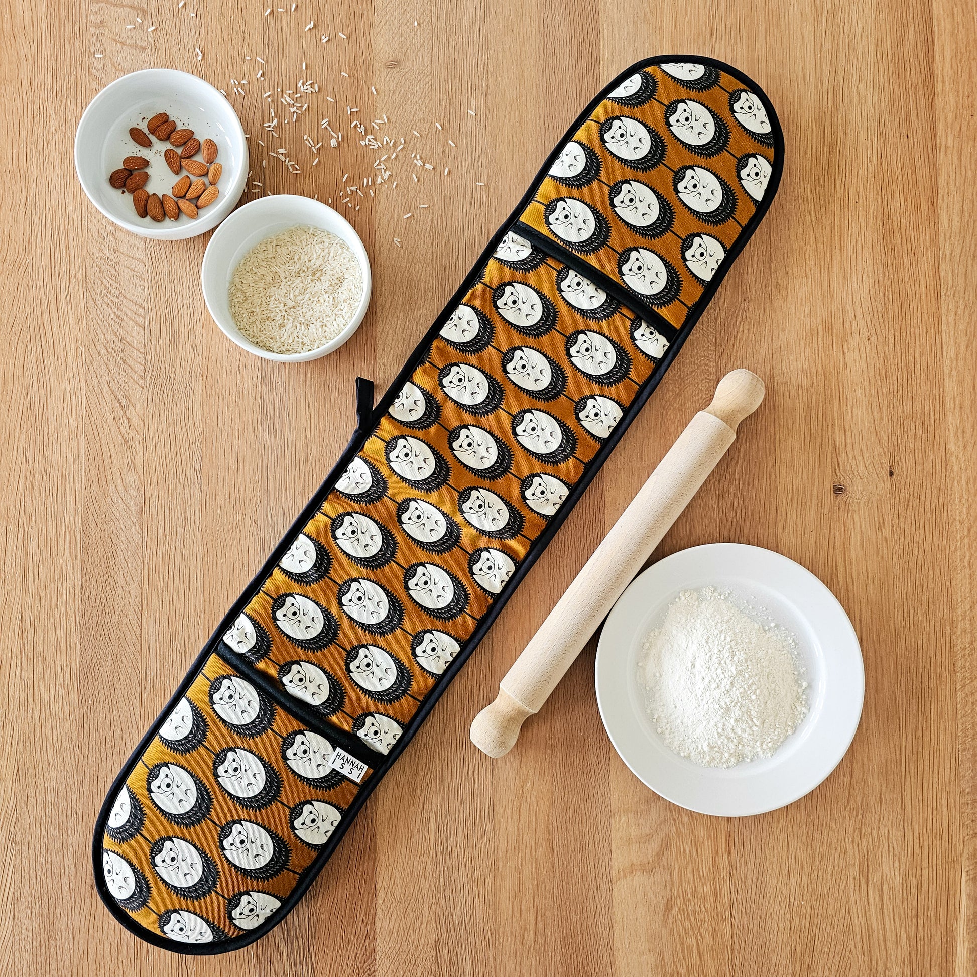 Organic cotton brown and white hedgehog double oven glove – handmade in the UK by Hannah Issi. Stylish, heat-safe kitchen accessory. Lifestyle image laying on wooden tabletop with cooking ingredients.