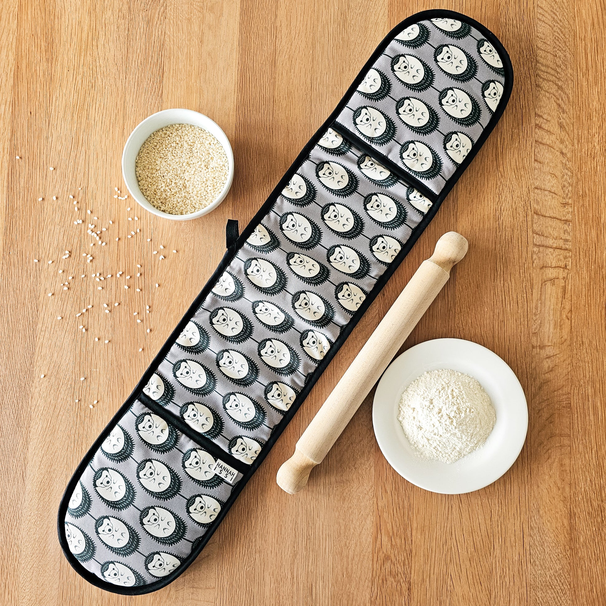 Organic cotton grey & white hedgehog double oven glove – handmade in the UK by Hannah Issi. Stylish, heat-safe kitchen accessory. Lifestyle image with cooking ingredients and rolling pin on wooden tabletop.