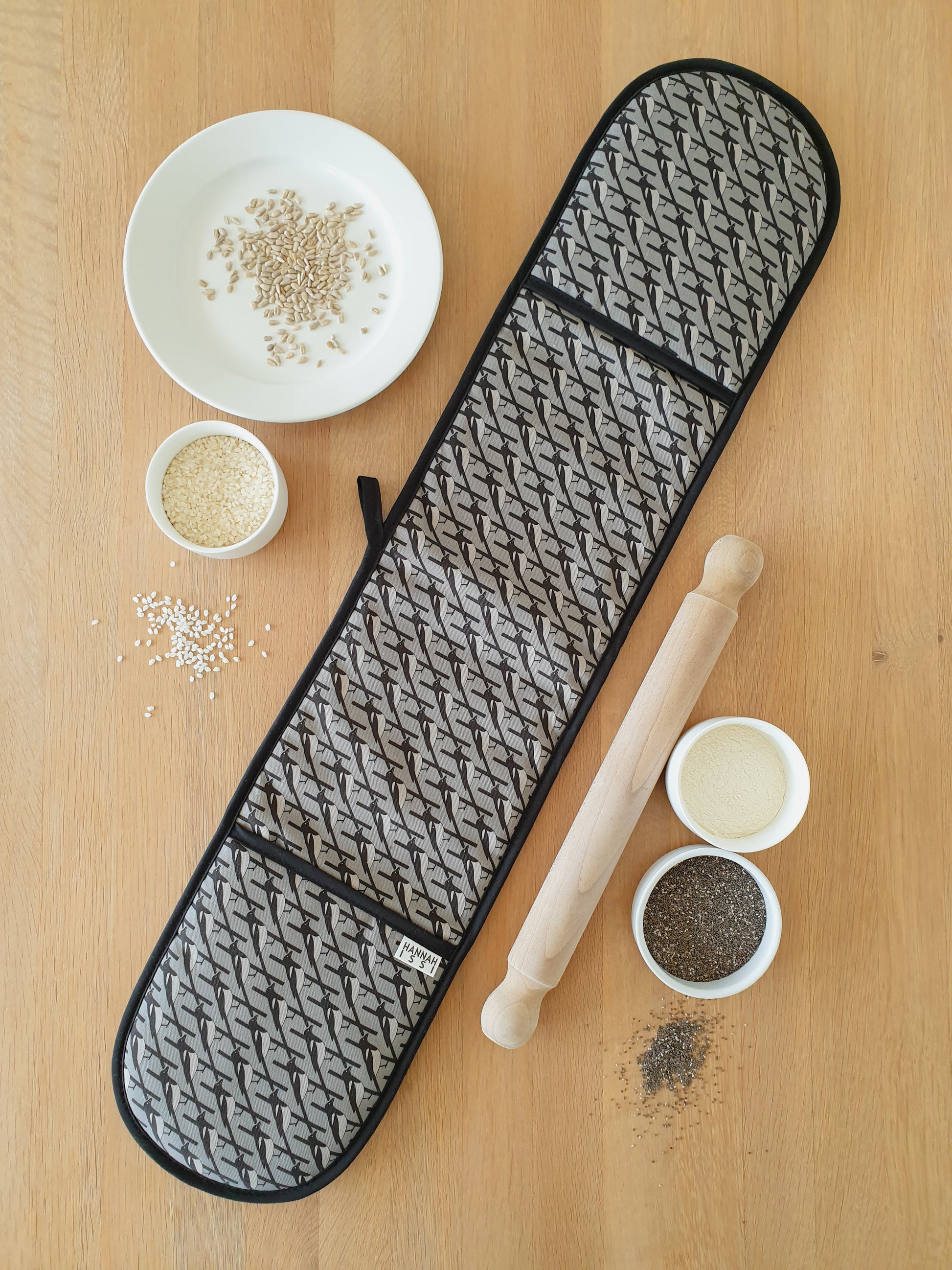 Organic cotton grey magpie double oven glove – handmade in the UK by Hannah Issi. Stylish, heat-safe kitchen accessory. Lifestyle image with wooden background and cooking ingredients. 