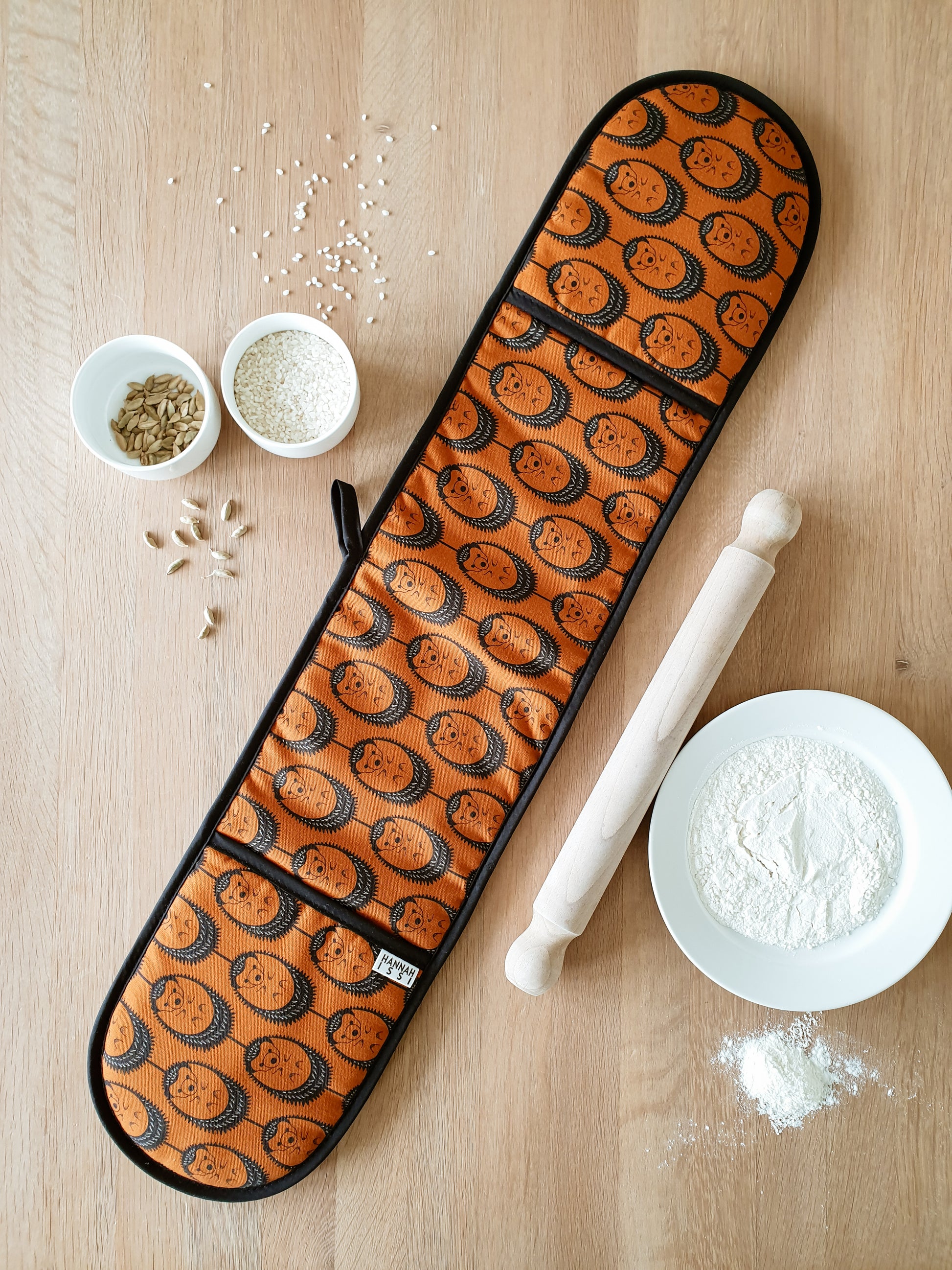 Organic cotton terracotta hedgehog double oven glove – handmade in the UK by Hannah Issi. Stylish, heat-safe kitchen accessory. Lifestyle image with wooden background and cooking ingredients. 