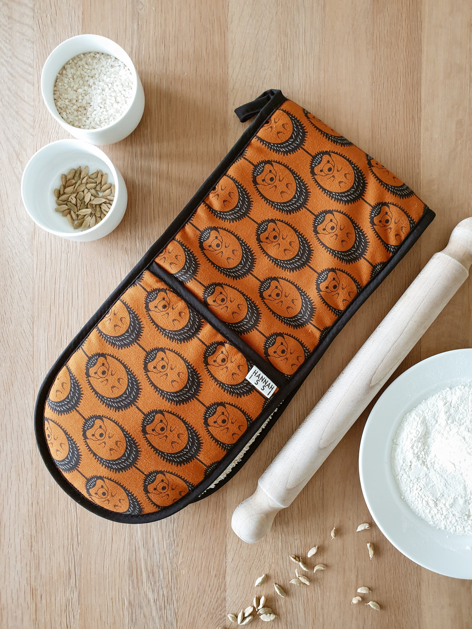 Organic cotton terracotta hedgehog double oven glove – handmade in the UK by Hannah Issi. Stylish, heat-safe kitchen accessory. Lifestyle image on wooden tabletop with cooking ingredients.