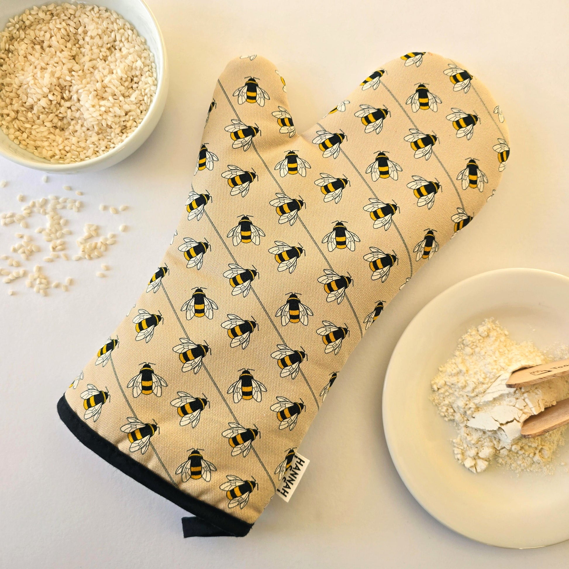 Organic cotton bee luxury oven glove – handmade in the UK by Hannah Issi. Stylish, heat-safe kitchen accessory. Lifestyle image with white background and cooking ingredients.