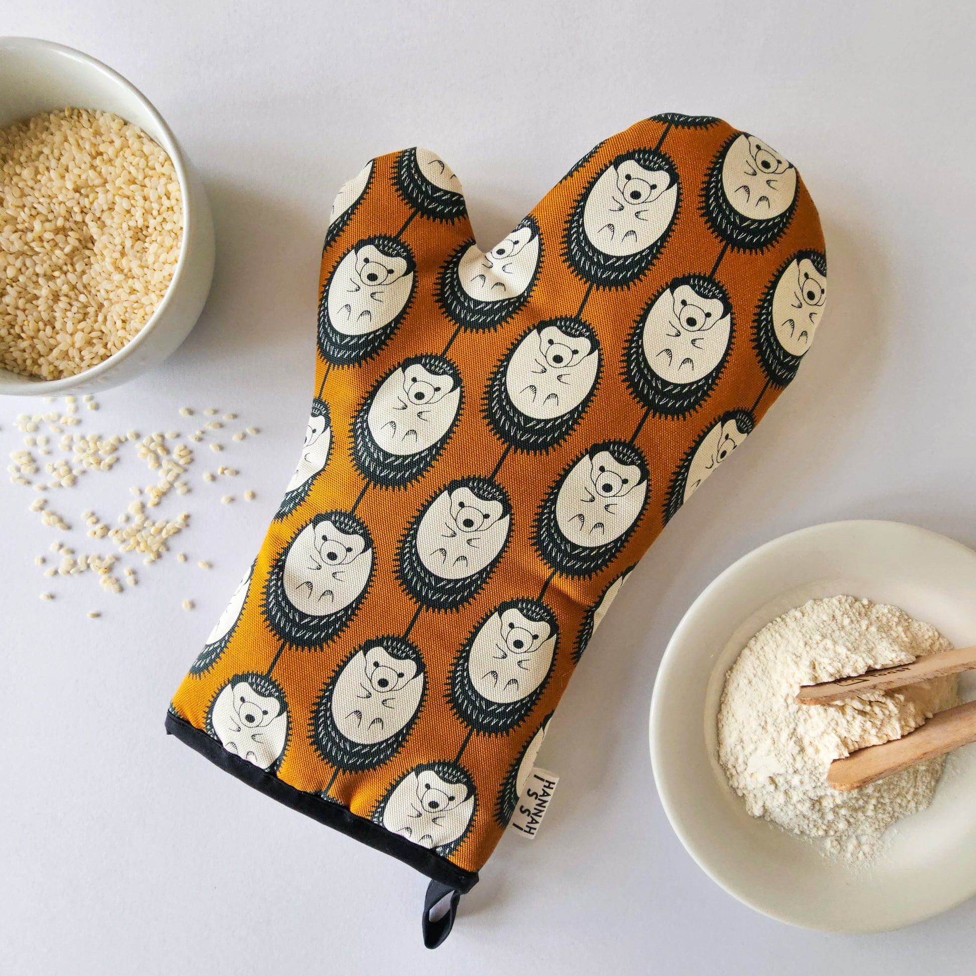 Organic cotton brown & white hedgehog luxury oven glove – handmade in the UK by Hannah Issi. Stylish, heat-safe kitchen accessory. Lifestyle image with white background and cooking ingredients.