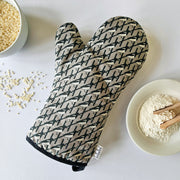 Organic cotton grey magpie luxury oven glove – handmade in the UK by Hannah Issi. Stylish, heat-safe kitchen accessory. Lifestyle image with white background and cooking ingredients.


