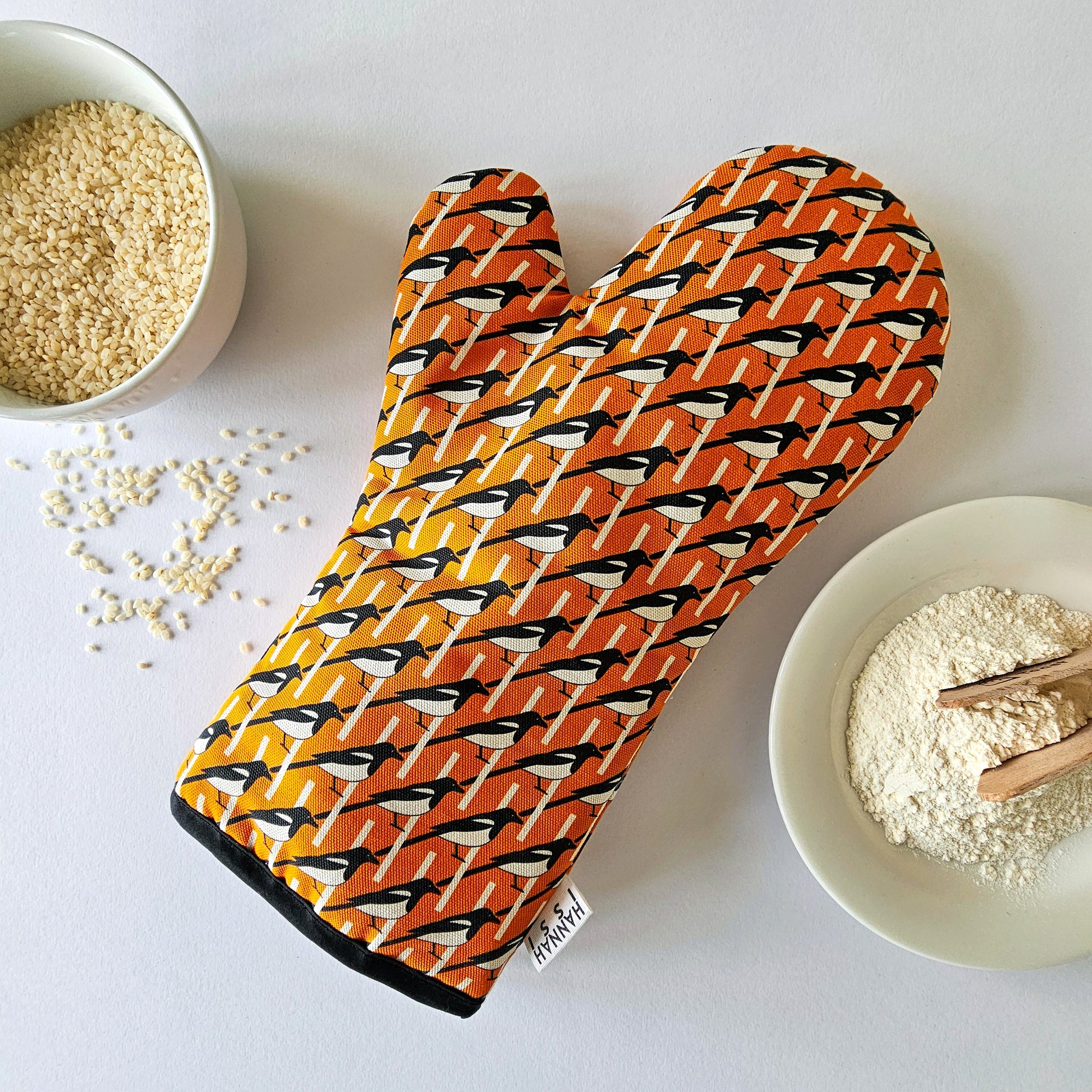 Organic cotton orange magpie luxury oven glove – handmade in the UK by Hannah Issi. Stylish, heat-safe kitchen accessory. Lifestyle image with white background and cooking ingredients.