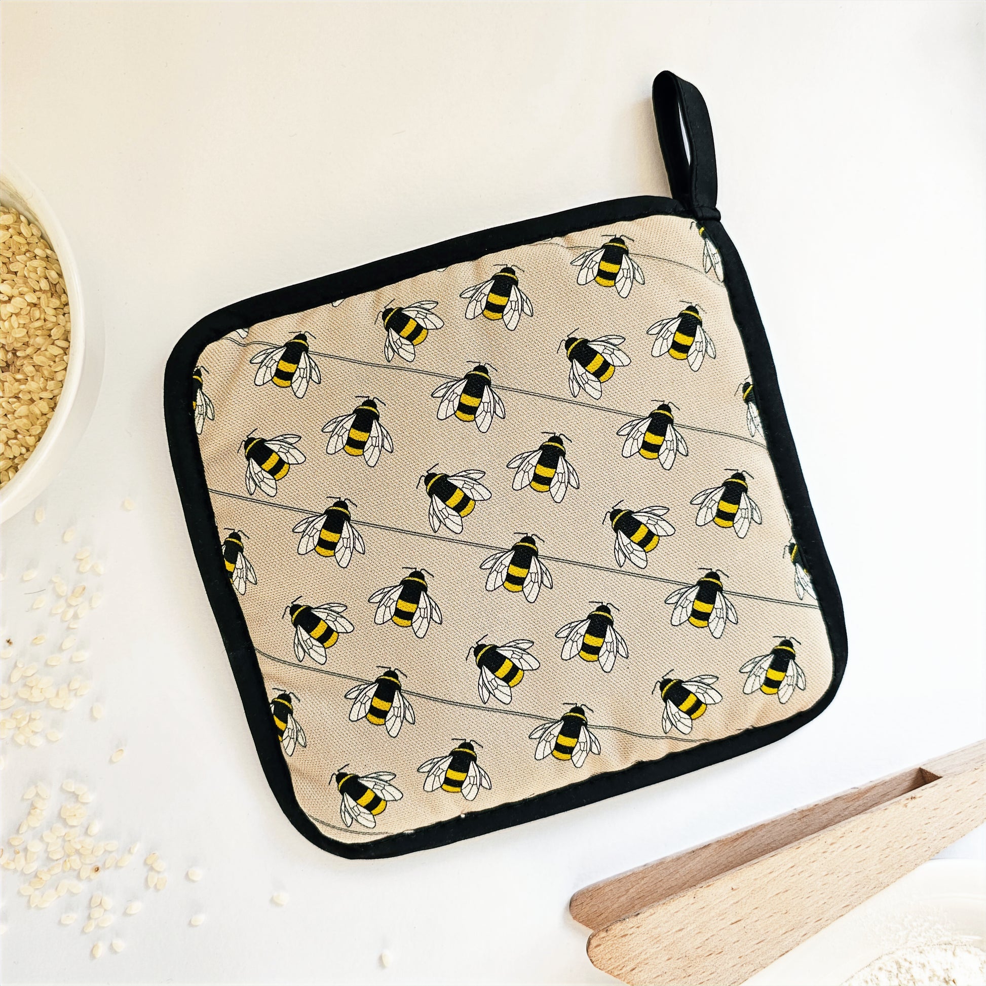 Organic cotton Bee pot grab – heat-safe kitchen handle cover by Hannah Issi, handmade in the UK. Stylish and functional. Image shows reverse of pot grab on white background with kitchen accessories.