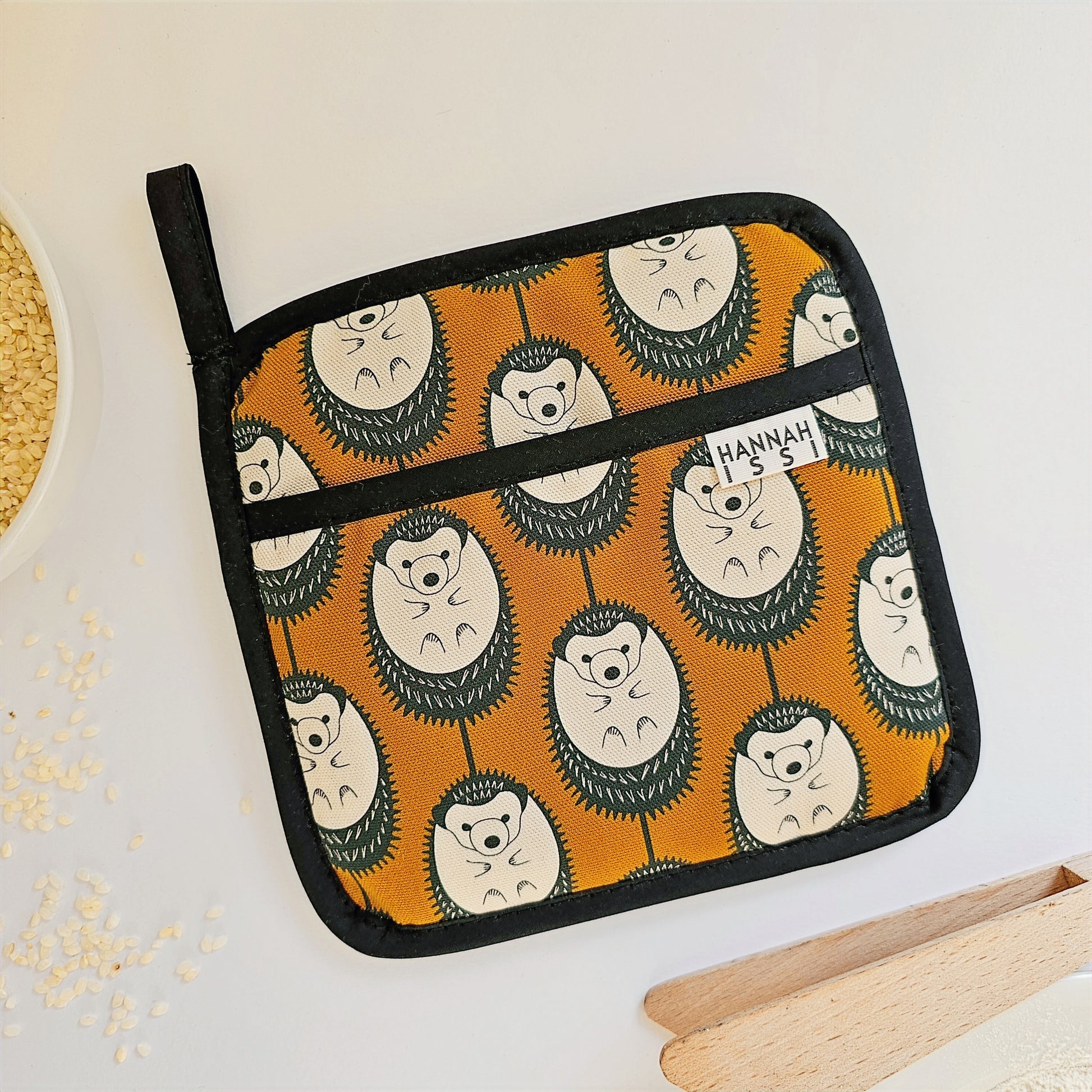 Organic cotton Brown & White Hedgehog pot grab – heat-safe kitchen handle cover by Hannah Issi, handmade in the UK. Stylish and functional. Lifestyle image on white background with kitchen accessories. 