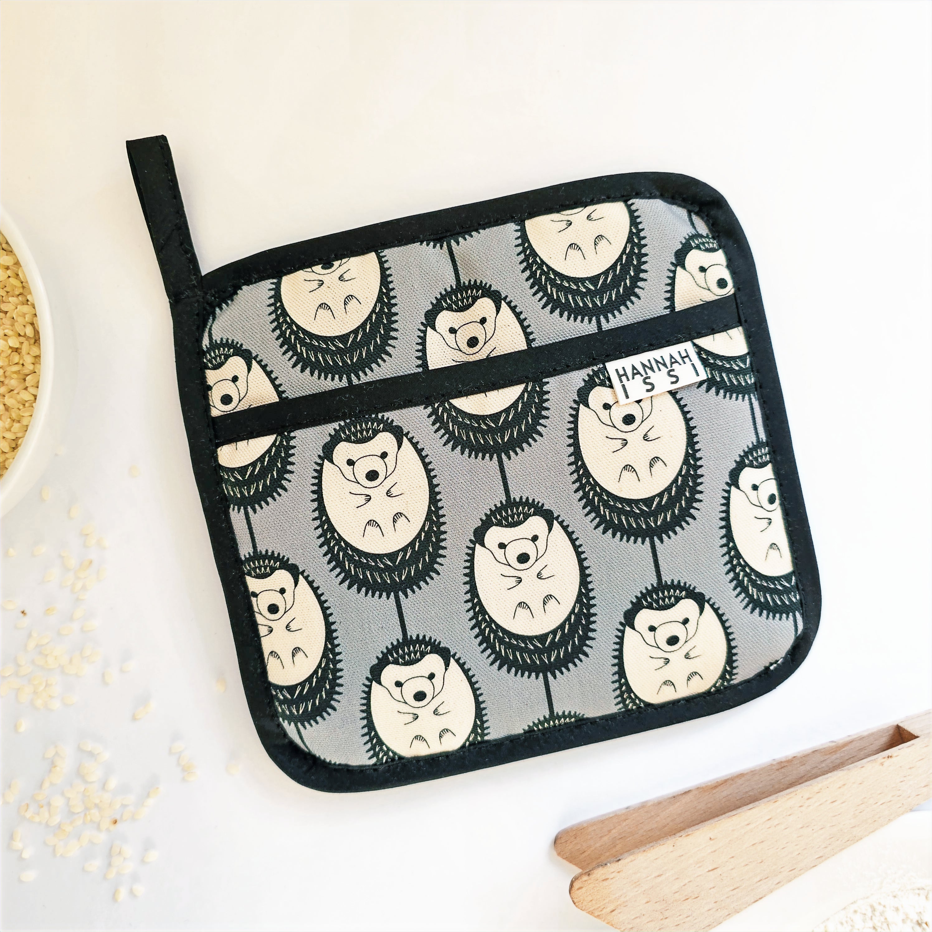 Organic cotton Grey & White Hedgehog  pot grab – heat-safe kitchen handle cover by Hannah Issi, handmade in the UK. Stylish and functional. Lifestyle image on white background and kitchen accessories. 