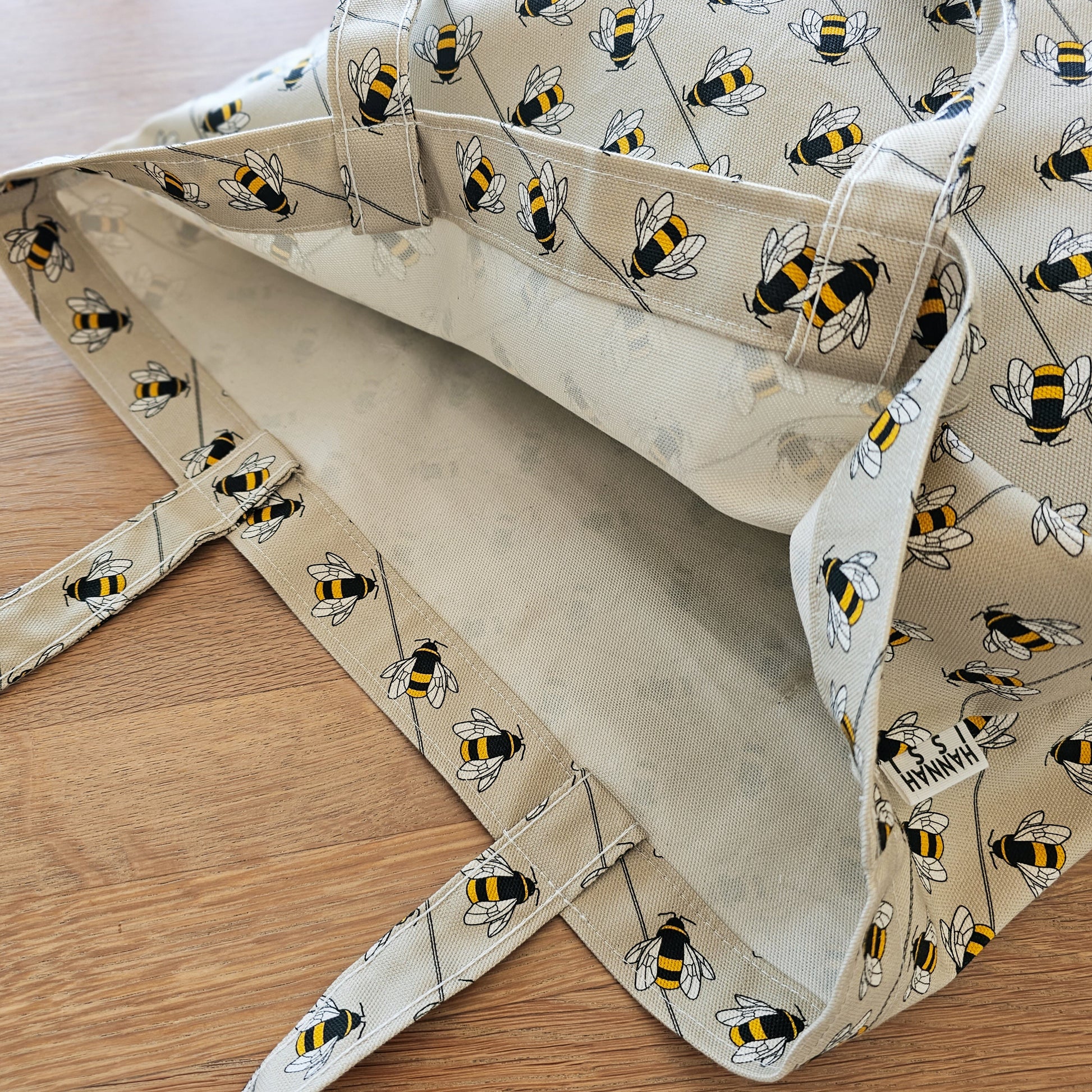 Organic cotton bee shoulder bag – handmade in the UK by Hannah Issi. Large, sustainable accessory for every day. Close-up showing bee print and strap detail on wooden tabletop. 