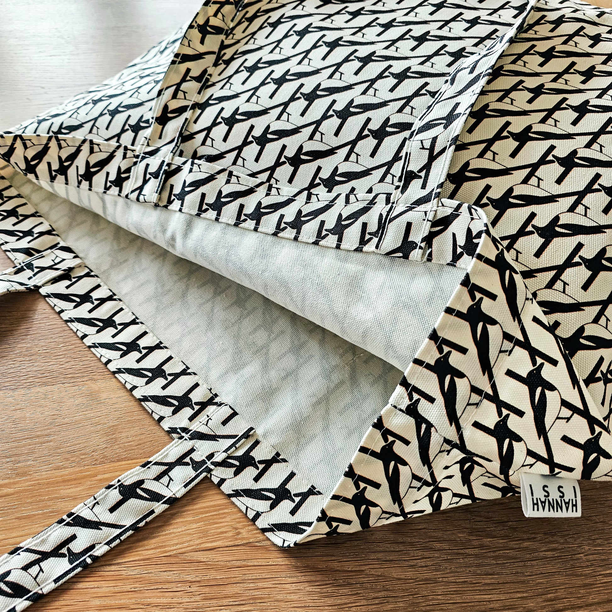 Organic cotton black & white Magpie shoulder bag – handmade in the UK by Hannah Issi. Large, sustainable accessory for every day. Close-up photo showing magpie print and strap detail laying on wooden table.