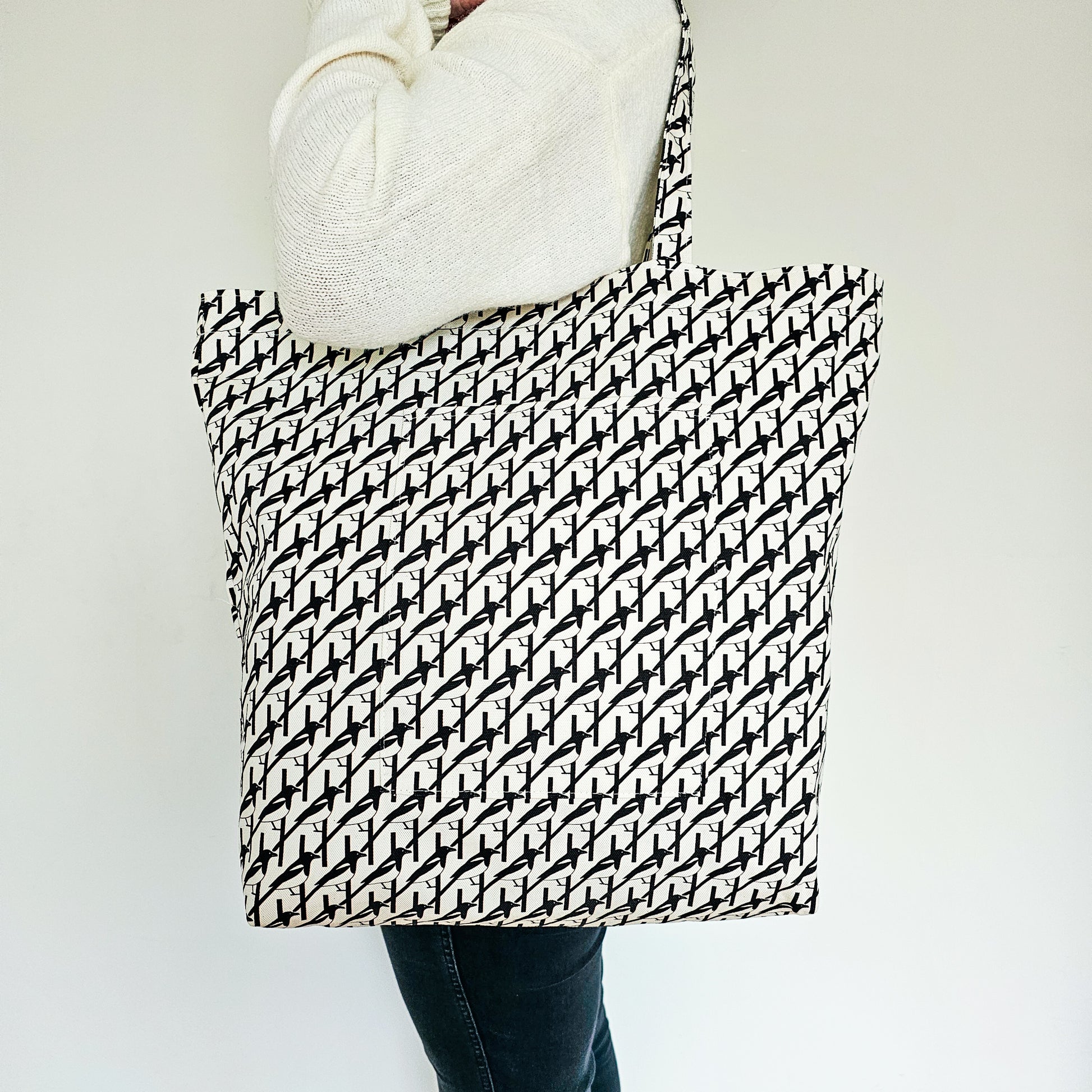 Organic cotton black & white Magpie shoulder bag – handmade in the UK by Hannah Issi. Large, sustainable accessory for every day. Bag shown modelled on shoulder with neutral background.