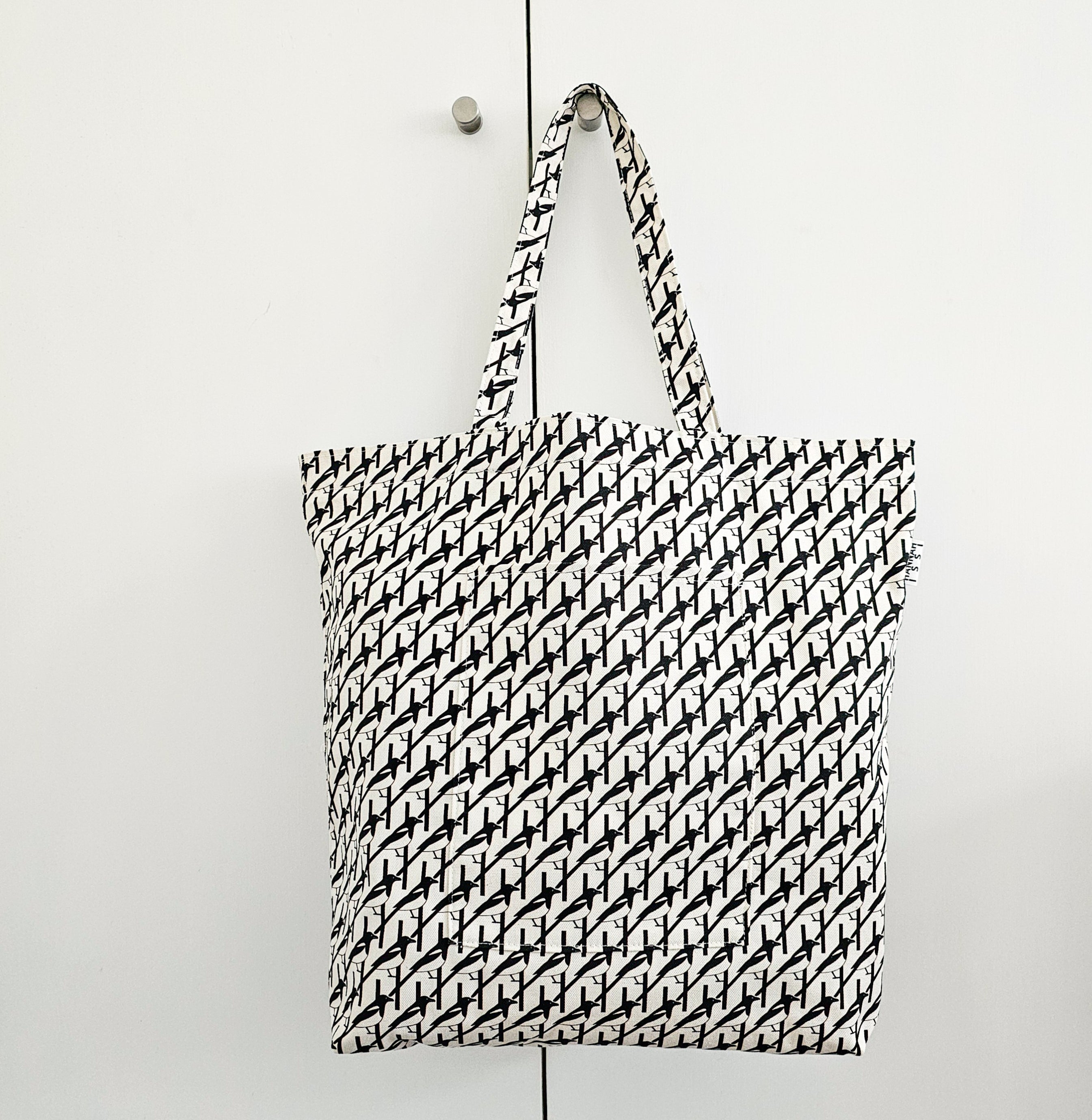 Organic cotton black & white Magpie shoulder bag – handmade in the UK by Hannah Issi. Large, sustainable accessory for every day shown hanging on white cupboard doors from doorknob.
