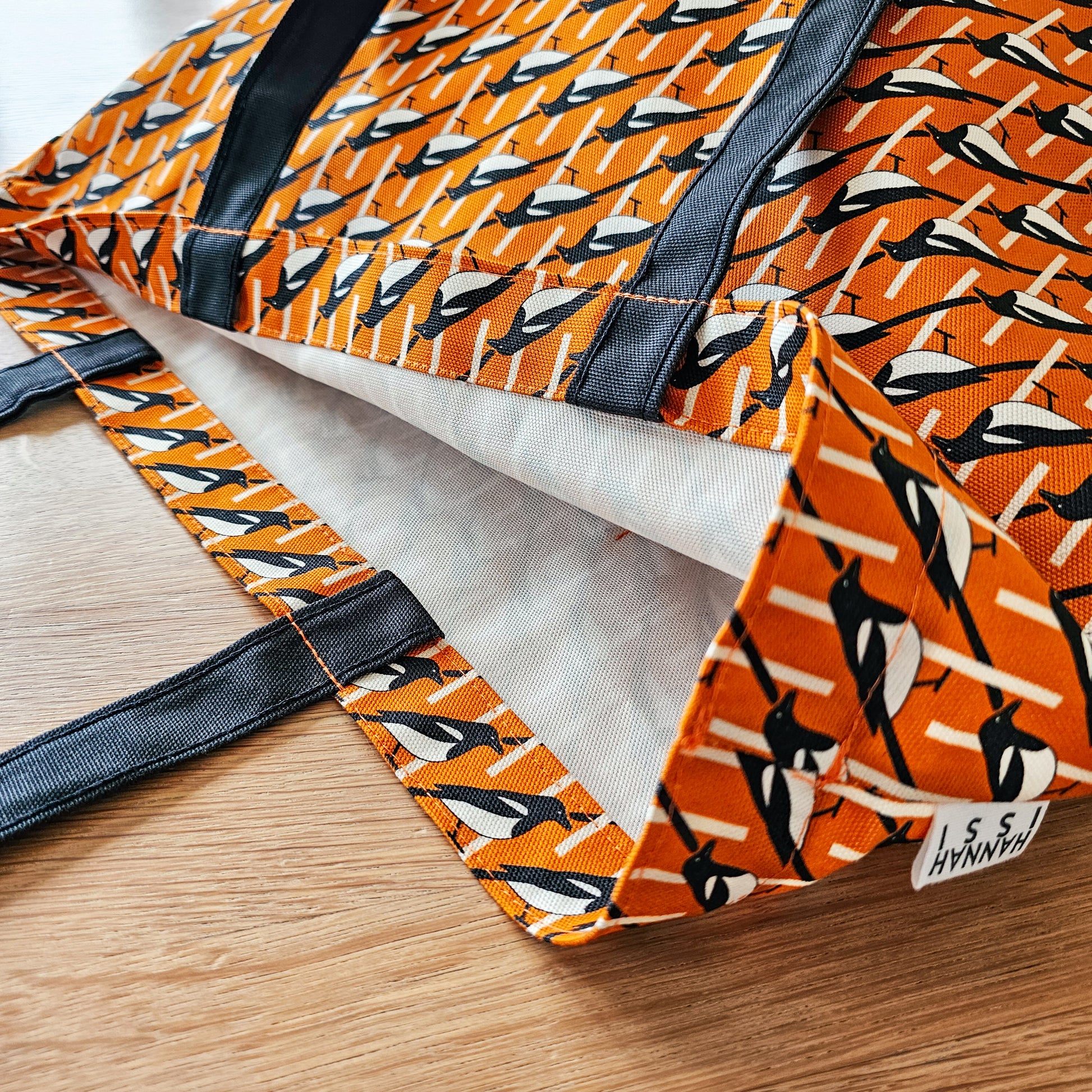 Organic cotton orange Magpie shoulder bag – handmade in the UK by Hannah Issi. Large, sustainable accessory for every day. Close-up photo showing print and strap detail on wooden tabletop.