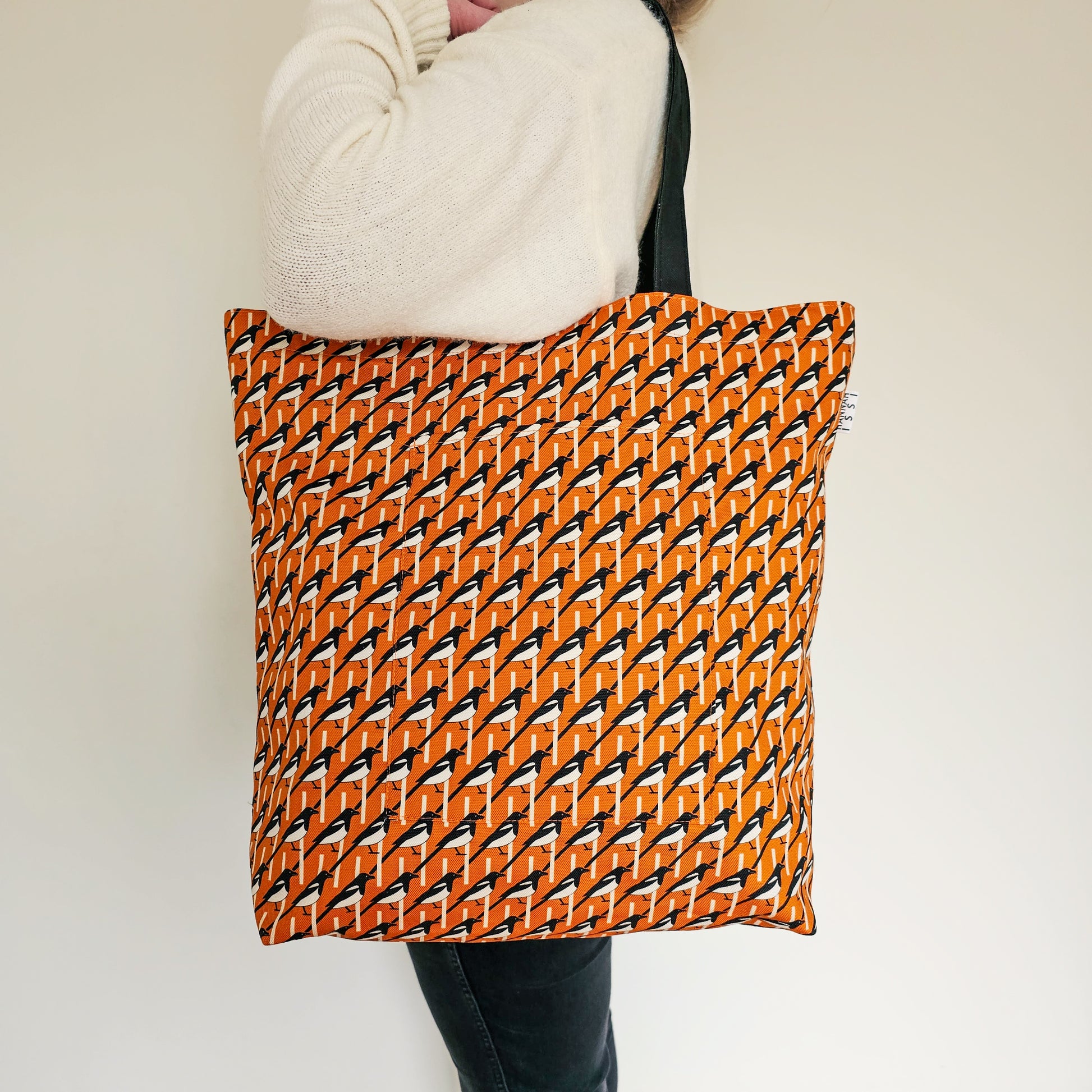 Organic cotton orange Magpie shoulder bag – handmade in the UK by Hannah Issi. Large, sustainable accessory for every day. Bag shown modelled on shoulder with neutral coloured background.