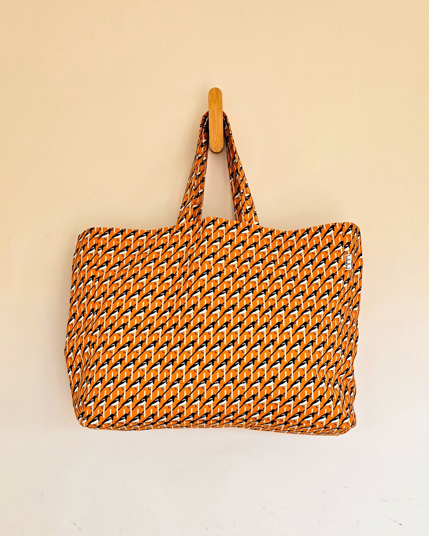 Organic cotton Magpie oversized shoulder bag – large, roomy design handmade in the UK by Hannah Issi. Stylish and sustainable. Bag is hanging on wooden hook with neutral coloured background.