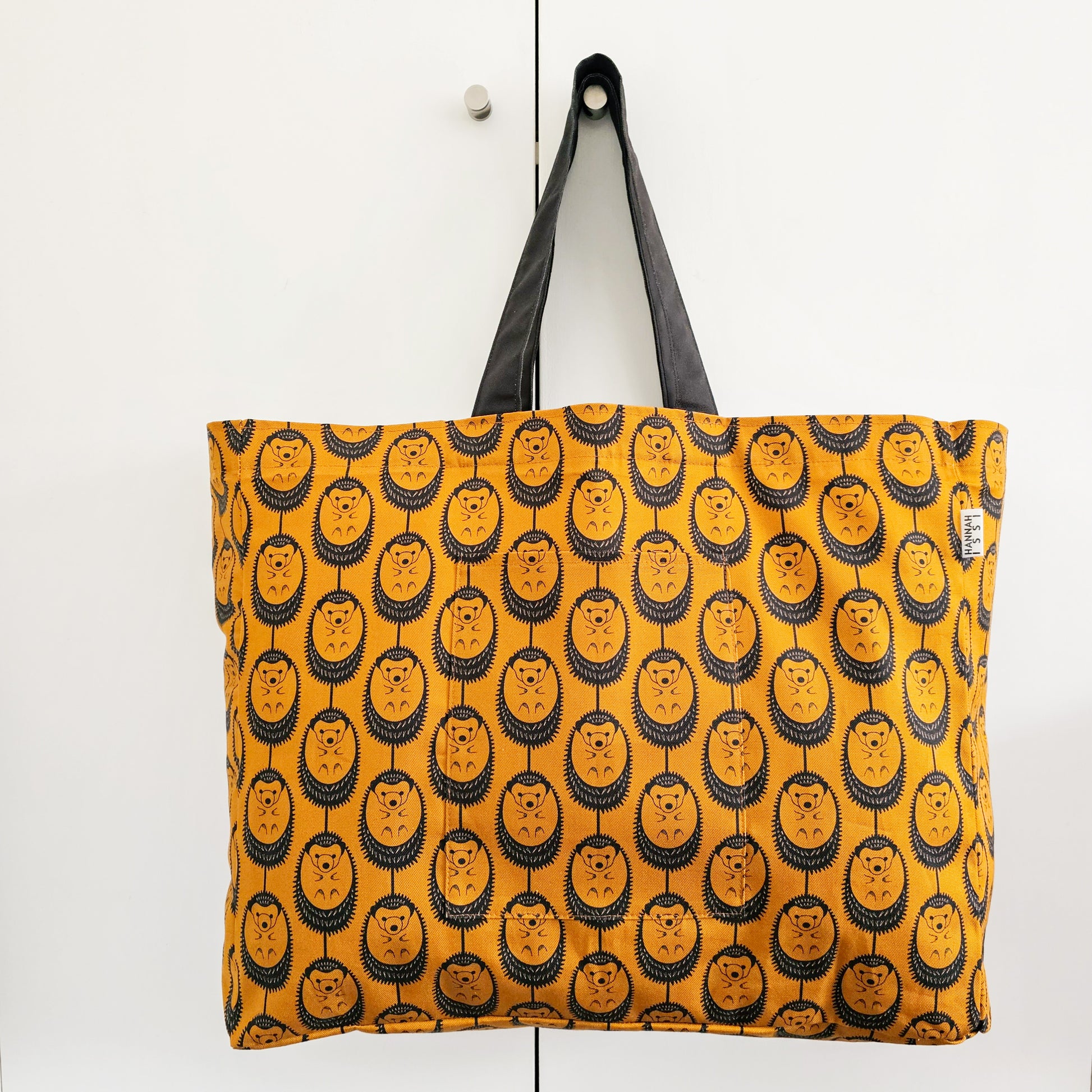 Organic cotton Ochre Hedgehog oversized shoulder bag – large, roomy design handmade in the UK by Hannah Issi. Stylish and sustainable. Bag is shown hanging on door knob with neutral background.