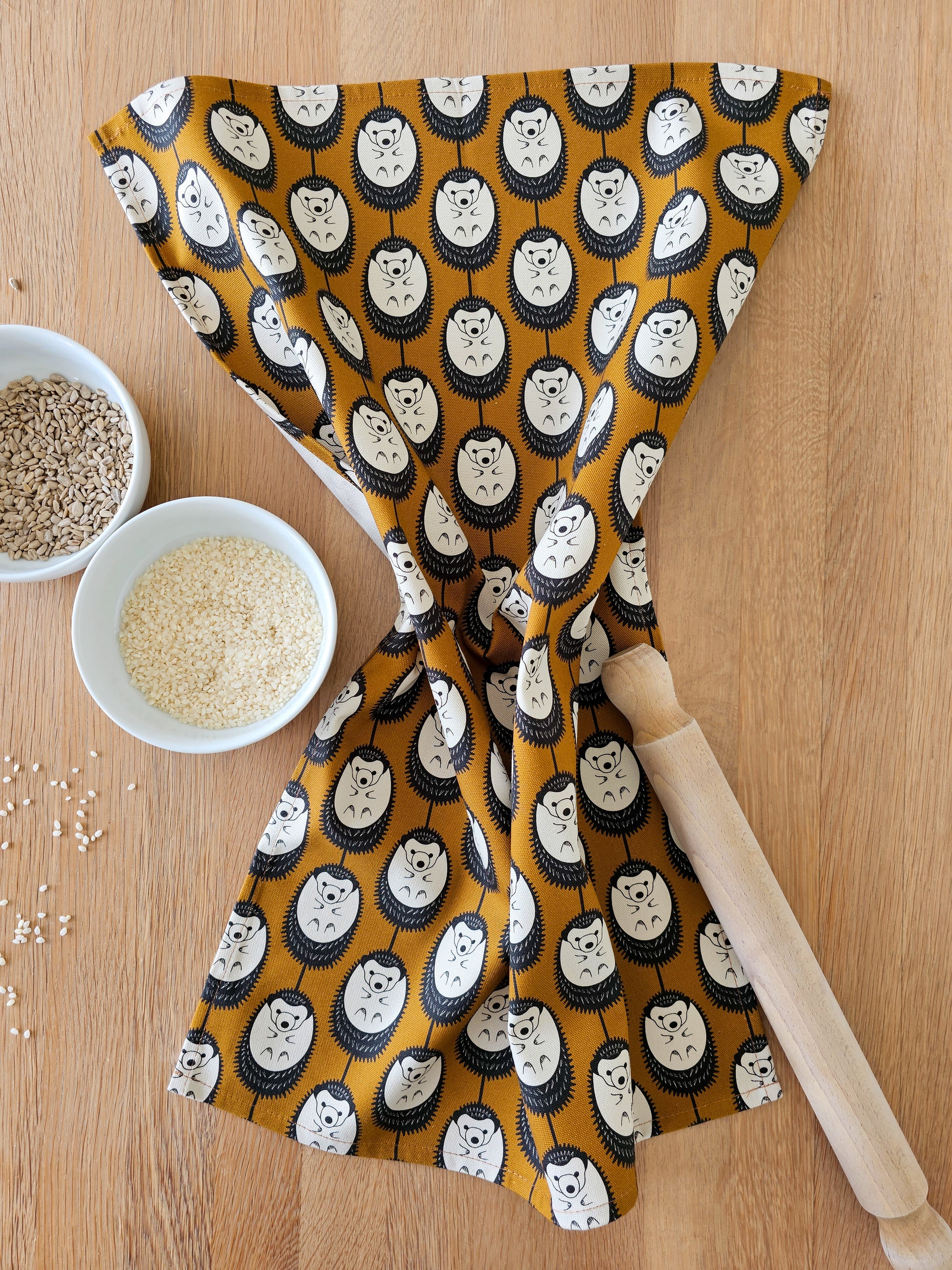 Organic cotton brown & white hedgehog tea towel – designed by Hannah Issi and handmade in the UK. Sustainable, modern and eco-friendly kitchen textile. Shown on wooden table with cooking ingredients. 