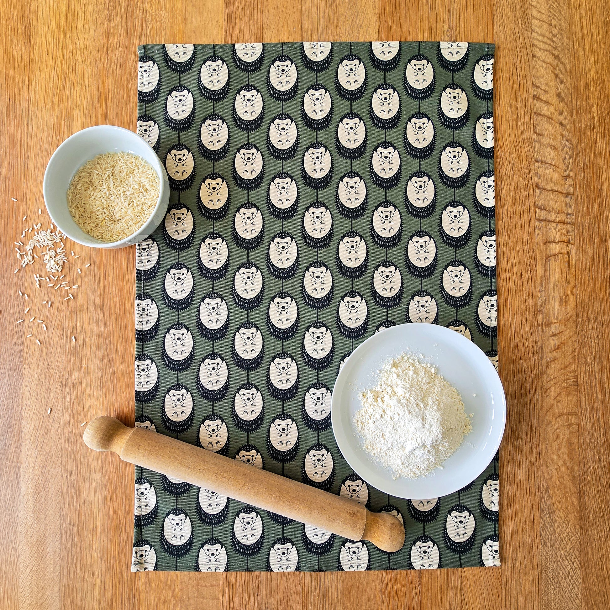 Organic cotton hedgehog tea towel in new green & white colour – designed by Hannah Issi and handmade in the UK. Sustainable, modern and eco-friendly kitchen textile. Tea towel on wooden table.