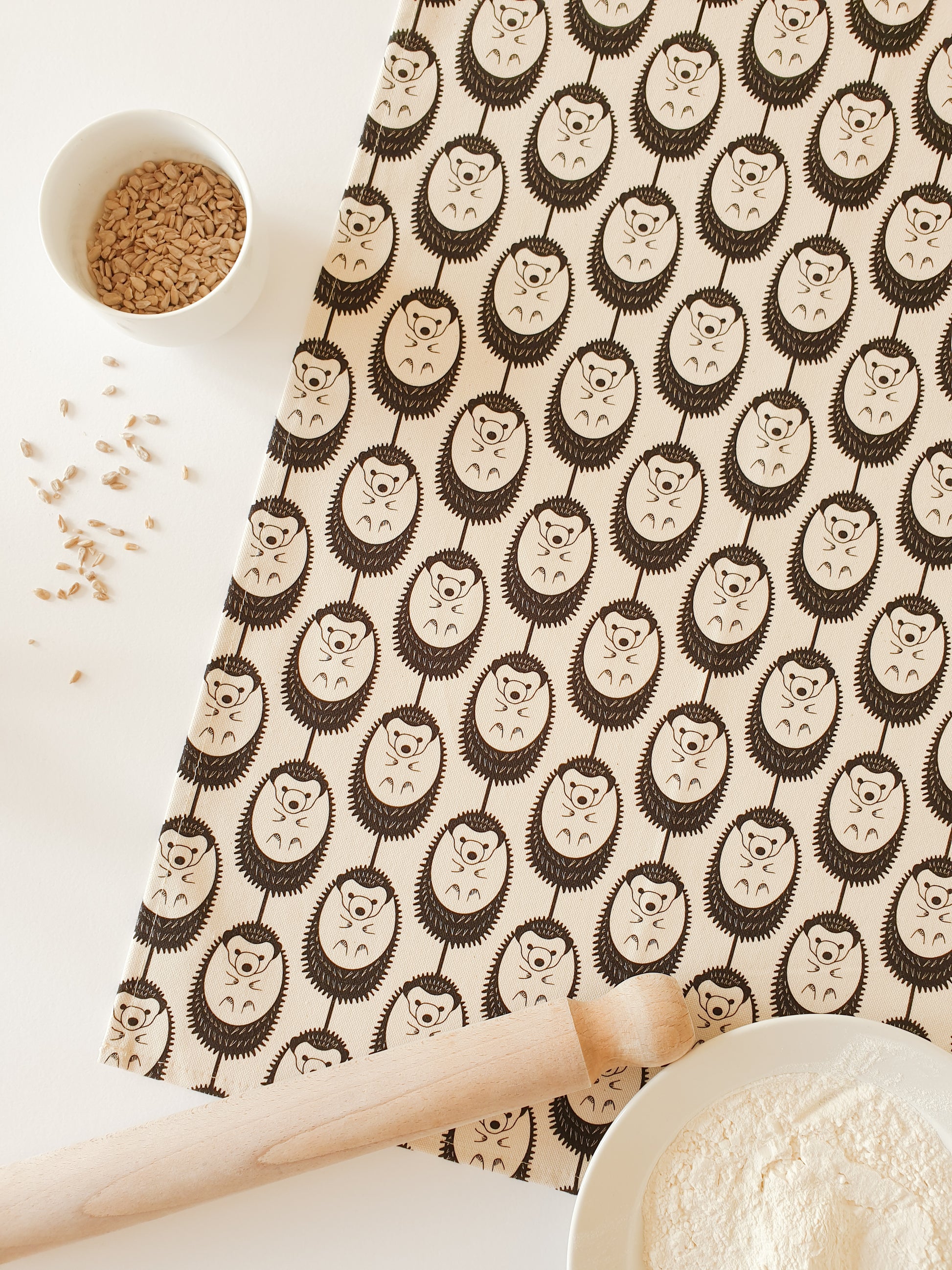 Organic cotton natural hedgehog tea towel – designed by Hannah Issi and handmade in the UK. Stylish, sustainable kitchen linen in neutral colour choice. Shown with a white background, rolling pin and cooking ingredients. 