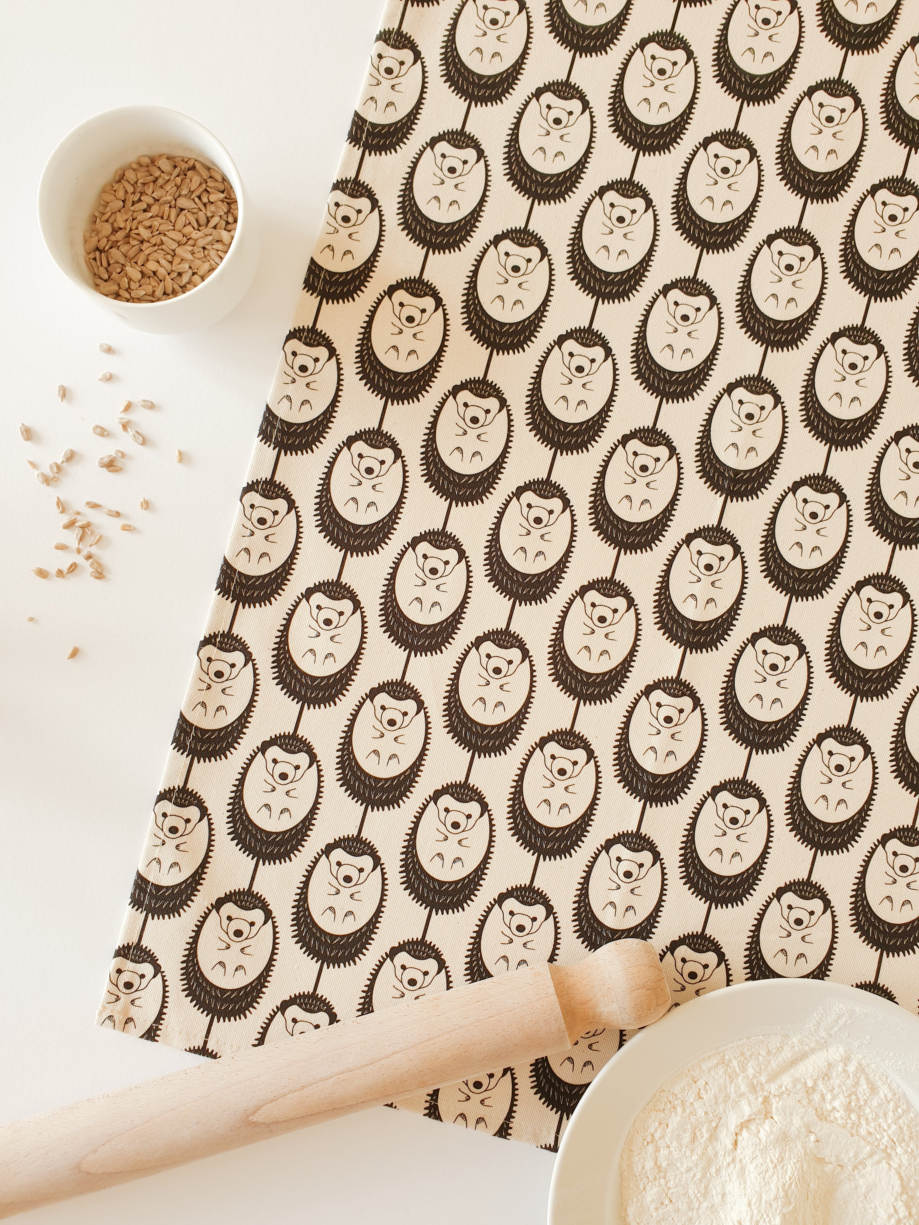 Organic cotton natural hedgehog tea towel – designed by Hannah Issi and handmade in the UK. Stylish, sustainable kitchen linen in neutral colour choice. Shown with a white background, rolling pin and cooking ingredients. 