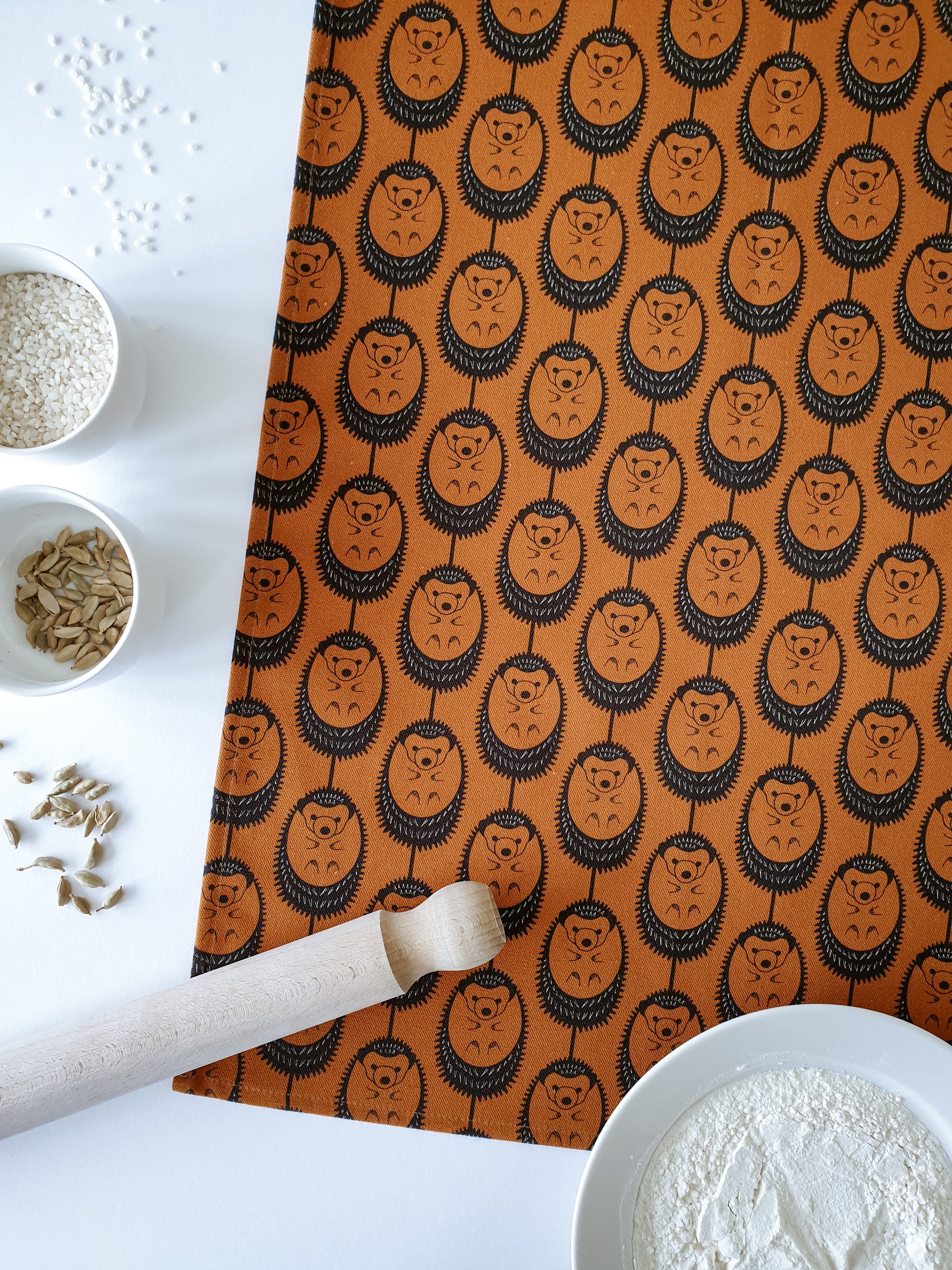 Organic cotton terracotta hedgehog tea towel – designed by Hannah Issi and handmade in the UK. Stylish, sustainable kitchen linen - shown with rolling pin and cooking ingredients. 