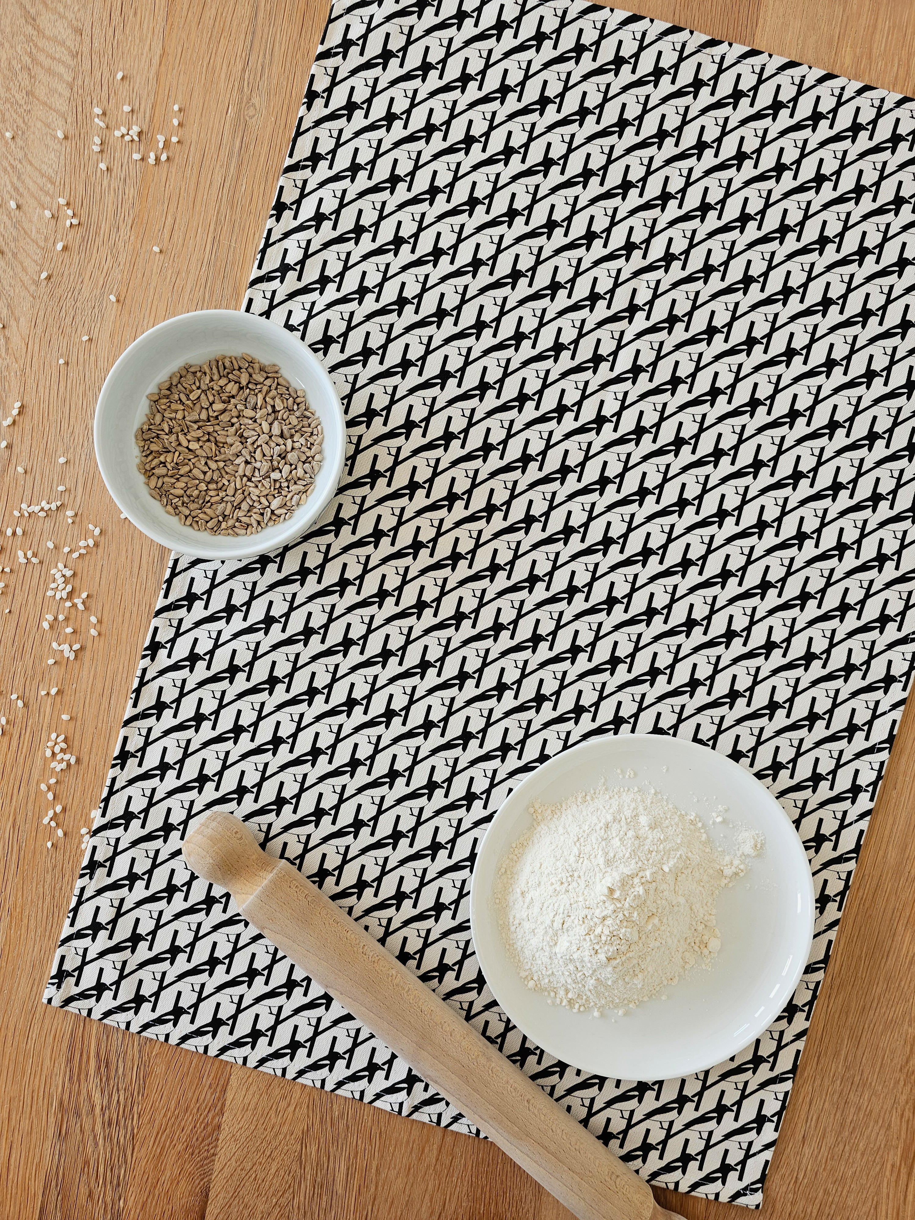 Organic cotton black and white magpie tea towel – designed by Hannah Issi and handmade in the UK. Stylish, sustainable kitchen linen - lifestyle image with wooden tabletop and cooking ingredients.