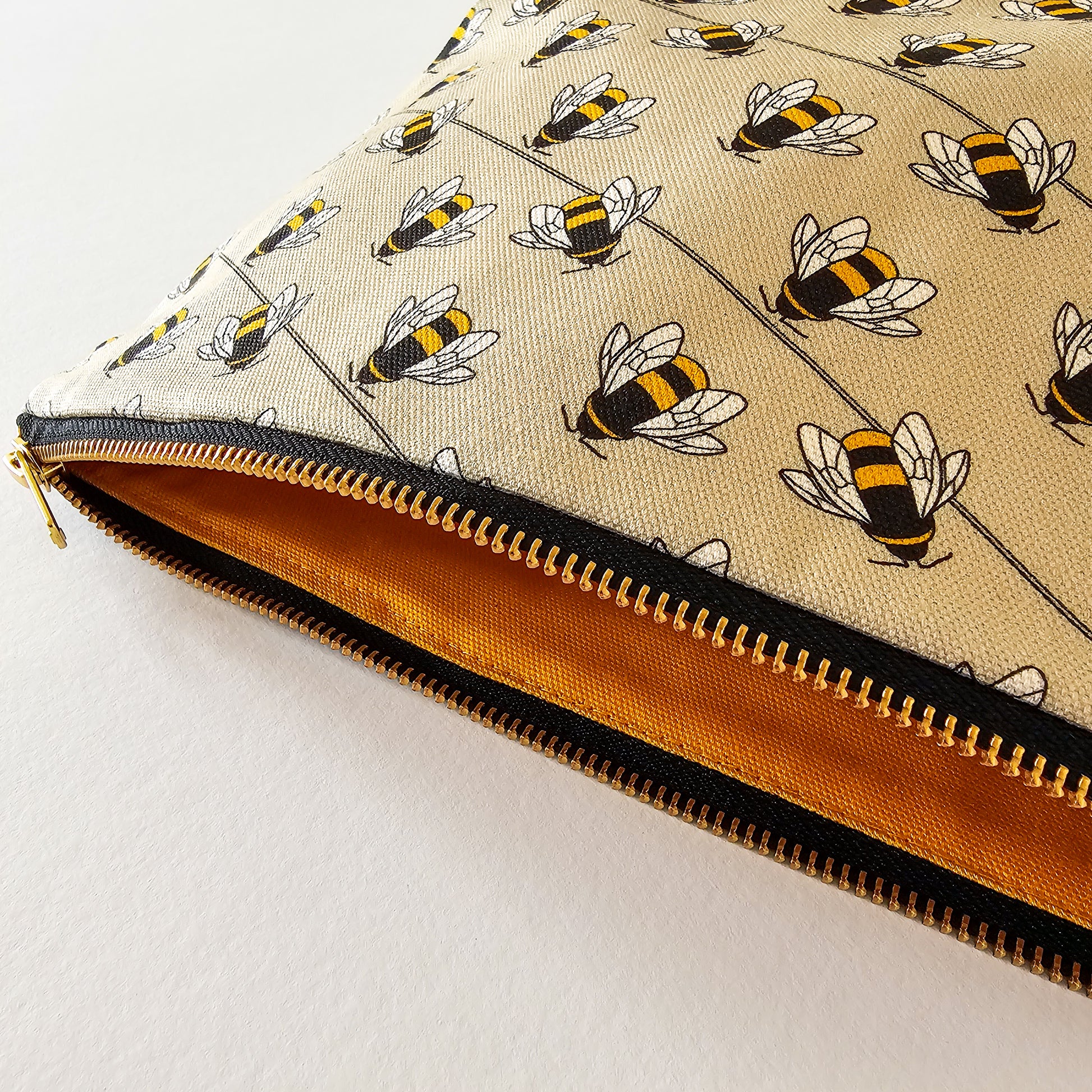 Organic cotton bee zip bag – handmade in the UK by Hannah Issi. Taupe bee print, versatile and sustainable accessory. Close-up photo showing brass zip and bee print.