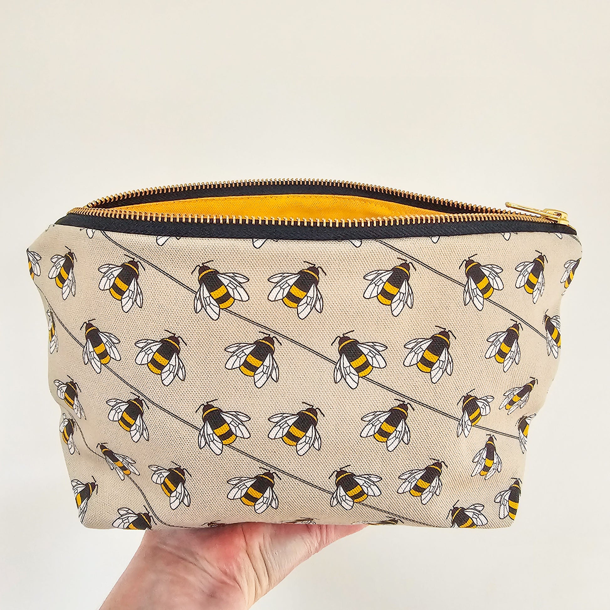 Organic cotton bee zip bag – handmade in the UK by Hannah Issi. Taupe bee print, versatile and sustainable accessory. Hand holding bag open with neutral background.