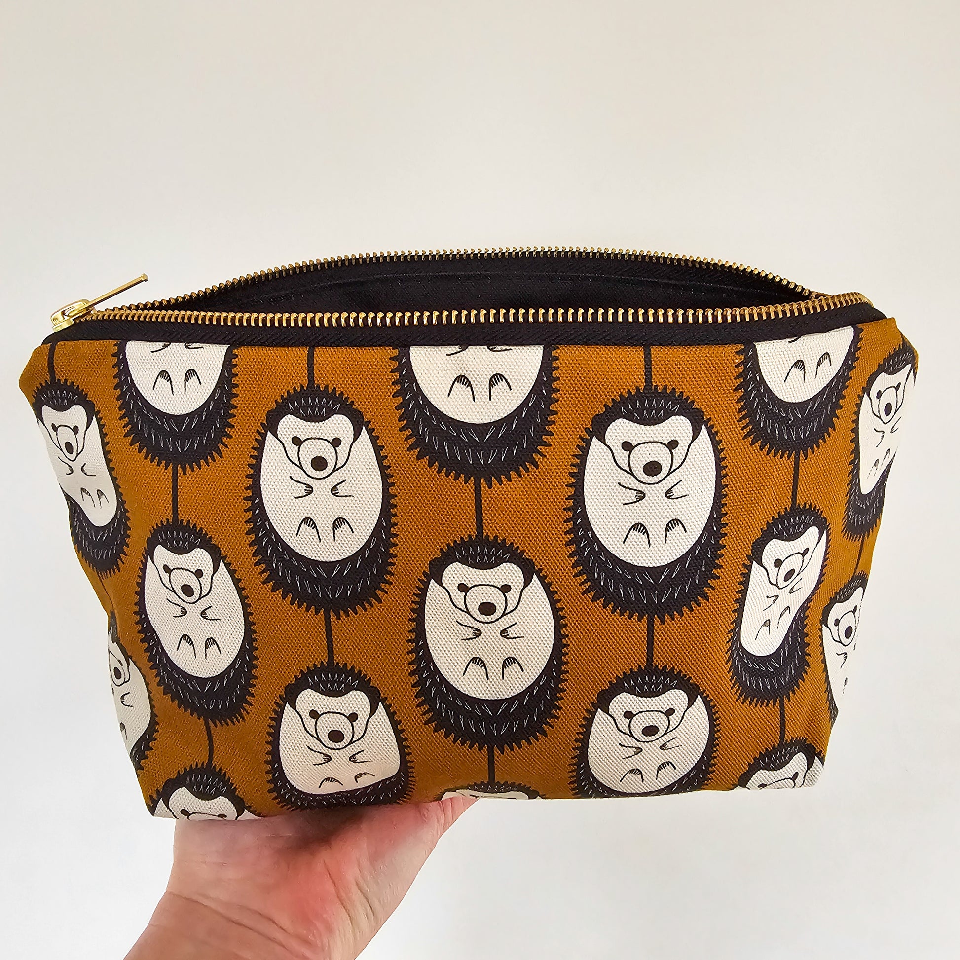 Organic cotton hedgehog zip bag – handmade in the UK by Hannah Issi. Brown & white hedgehog print, versatile and sustainable accessory. Hand holding bag open with neutral background.