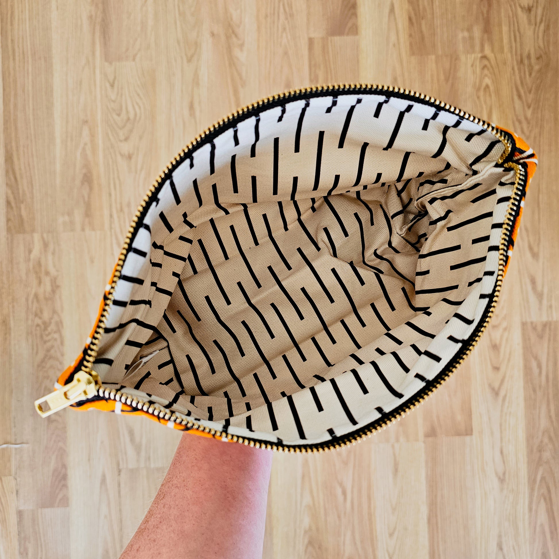 Organic cotton magpie zip bag – handmade in the UK by Hannah Issi. Orange magpie print, versatile and sustainable accessory. Hand holding bag open showing zip bag lining with wooden background. 